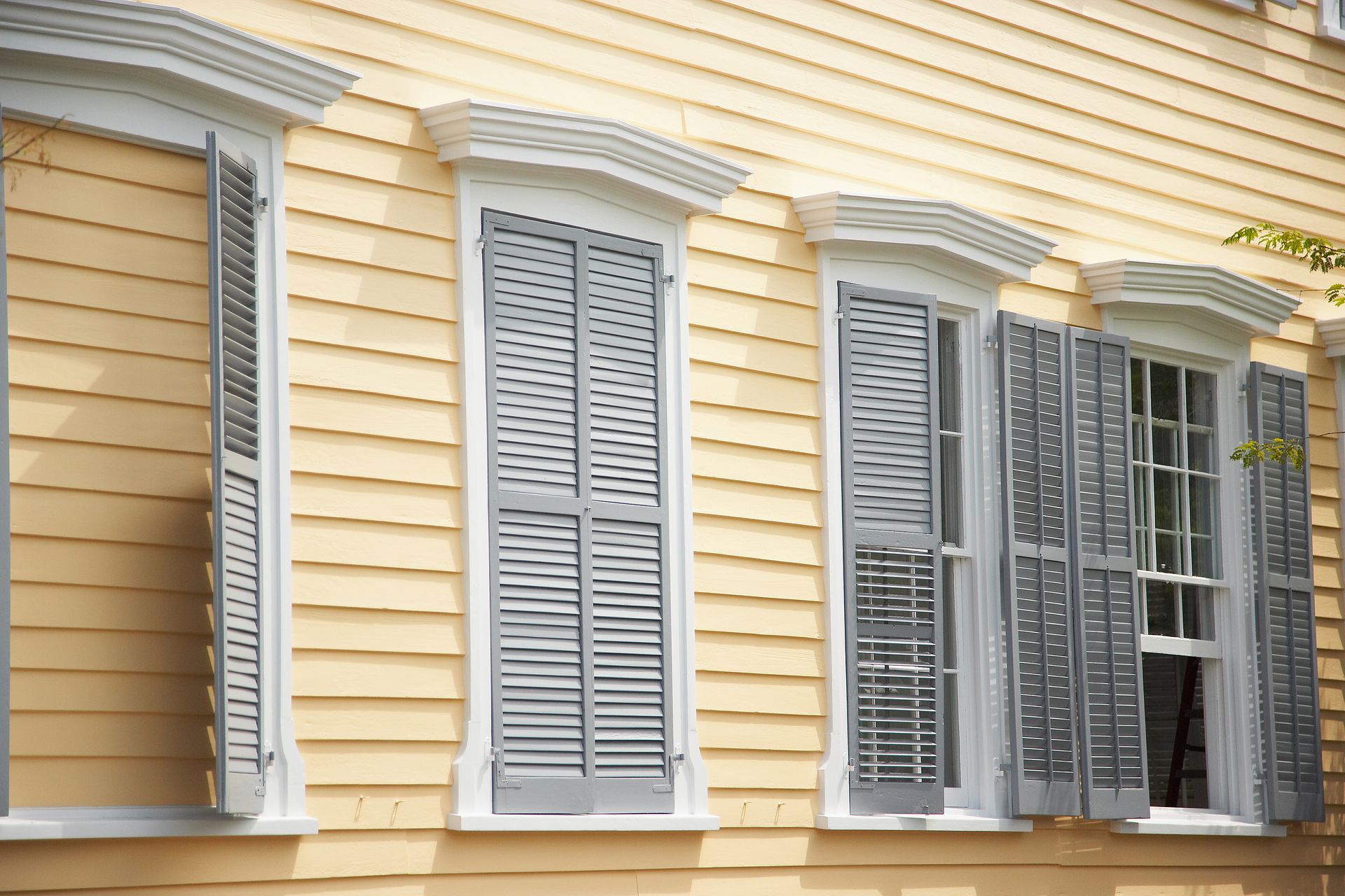 Yellow house with gray shutters on windows.