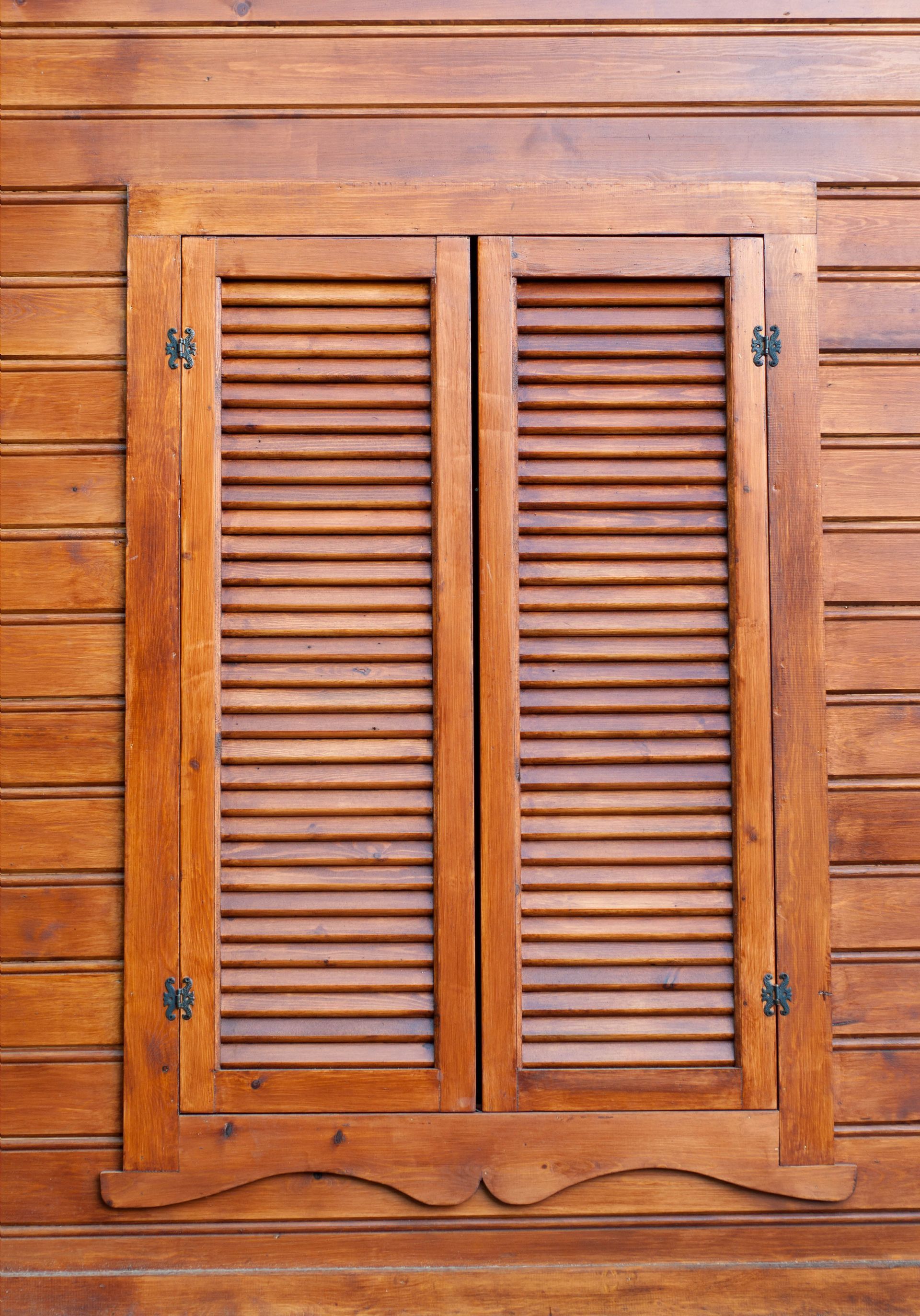 Wooden window shutters closed on a wood-paneled wall, warm brown tones.