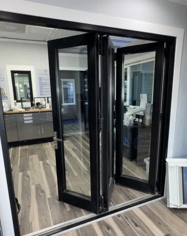 Black framed folding glass doors, hardwood floors, white trim. Display in a showroom.
