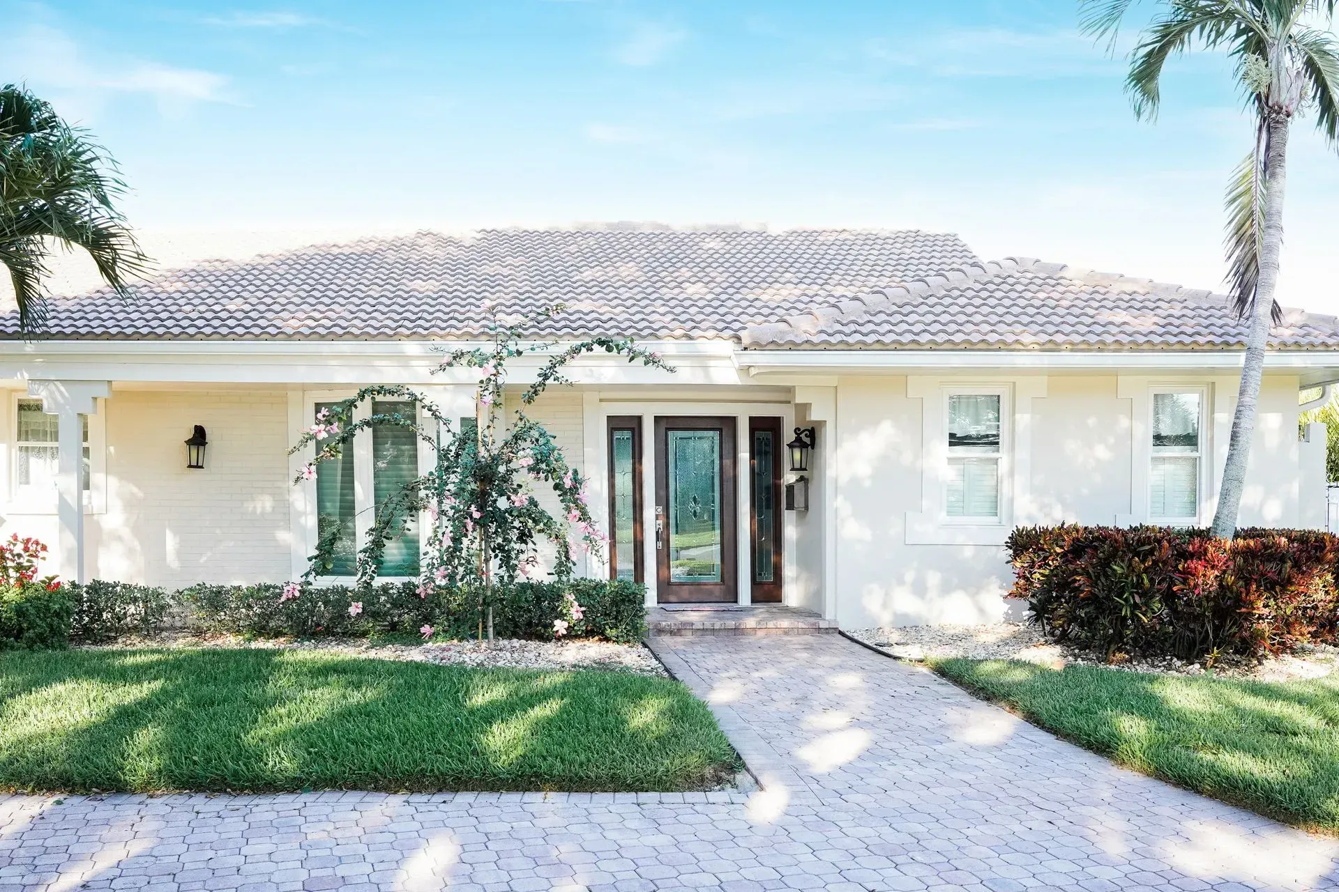 White house with a brick walkway and palm trees under a blue sky.