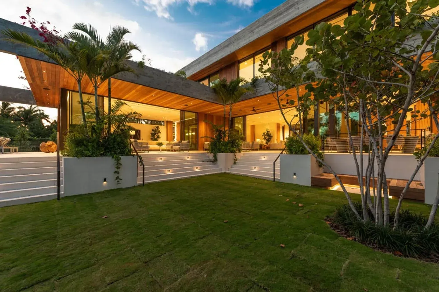 Modern home with wooden accents and large windows, surrounded by green grass and plants.