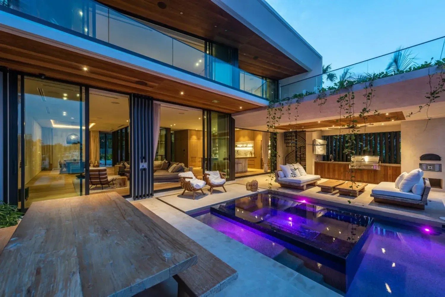Luxury modern home with pool, open-air patio, and second-story balcony, lit with purple pool lights.