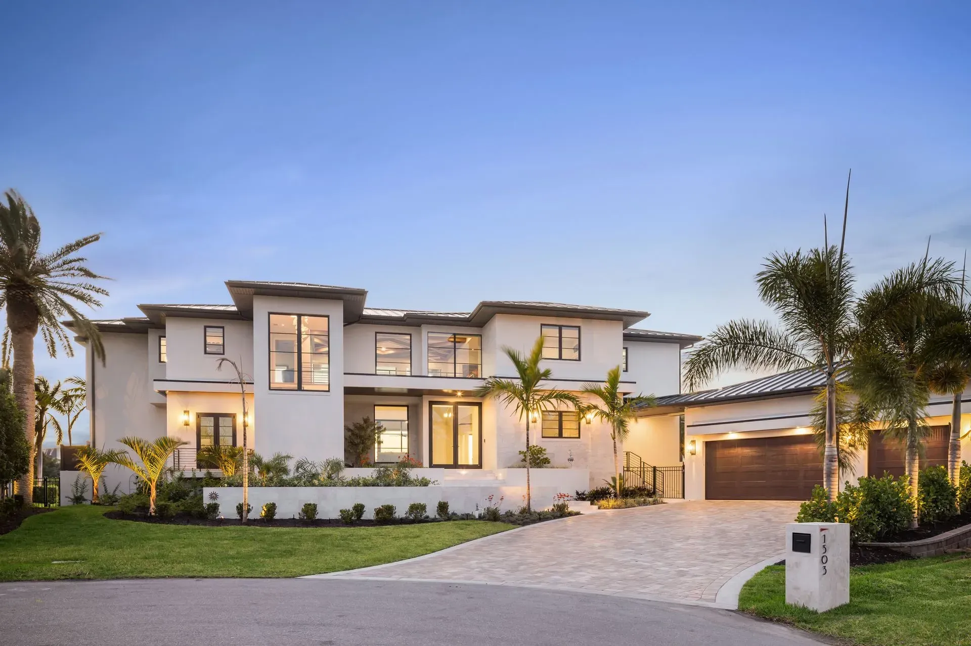 Two-story white stucco home with dark trim and arched driveway, palm trees.