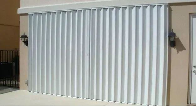 Accordion-style, white hurricane shutters closed on a beige building with black sconces.