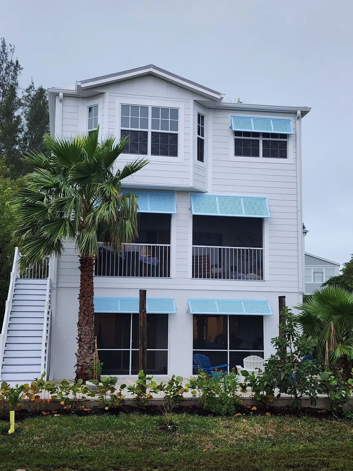 White three-story house with blue awnings and palm tree in front. Exterior stairs on the left.