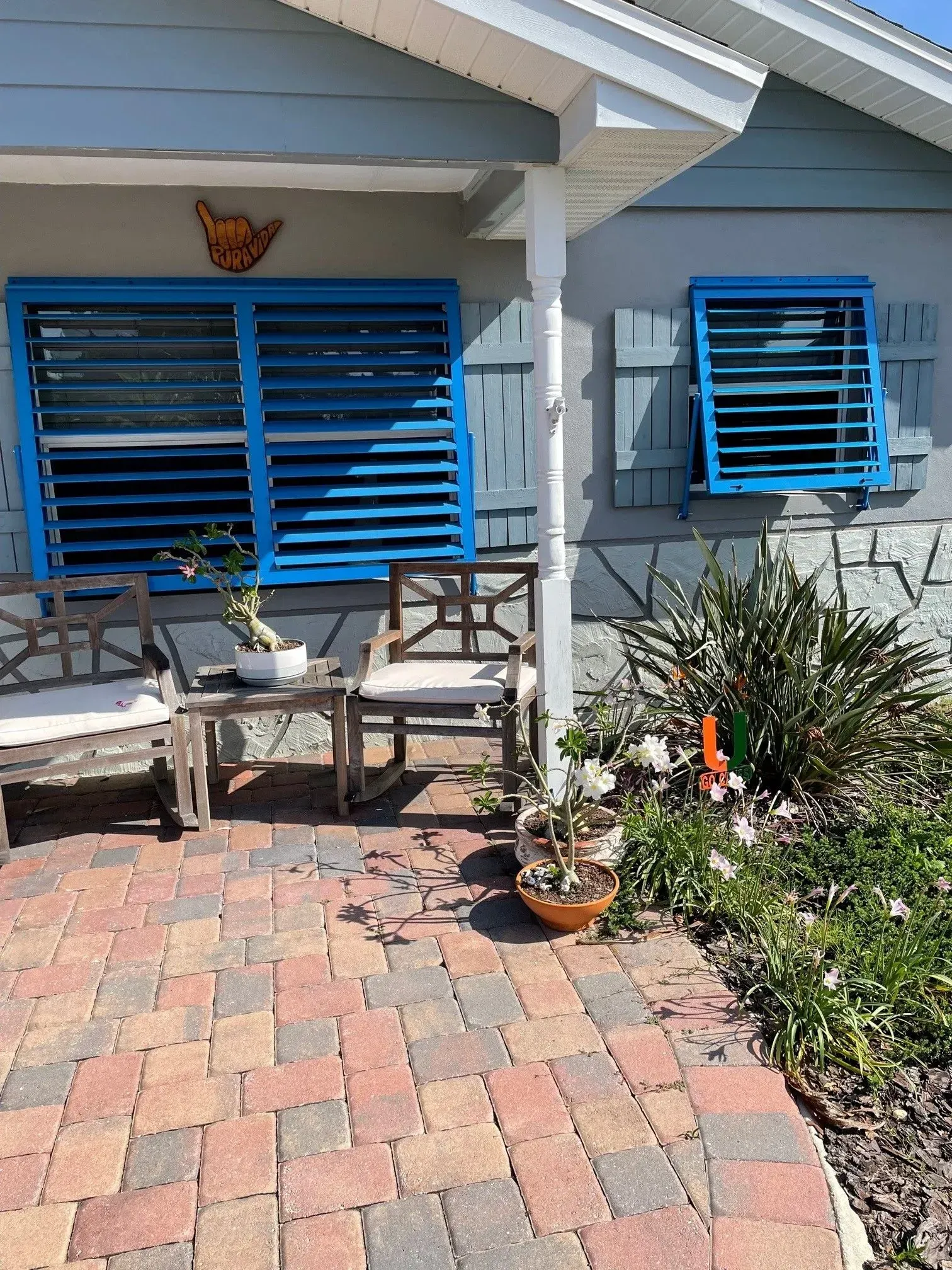 Blue shutters on a house with a brick patio, chairs, and potted plants.