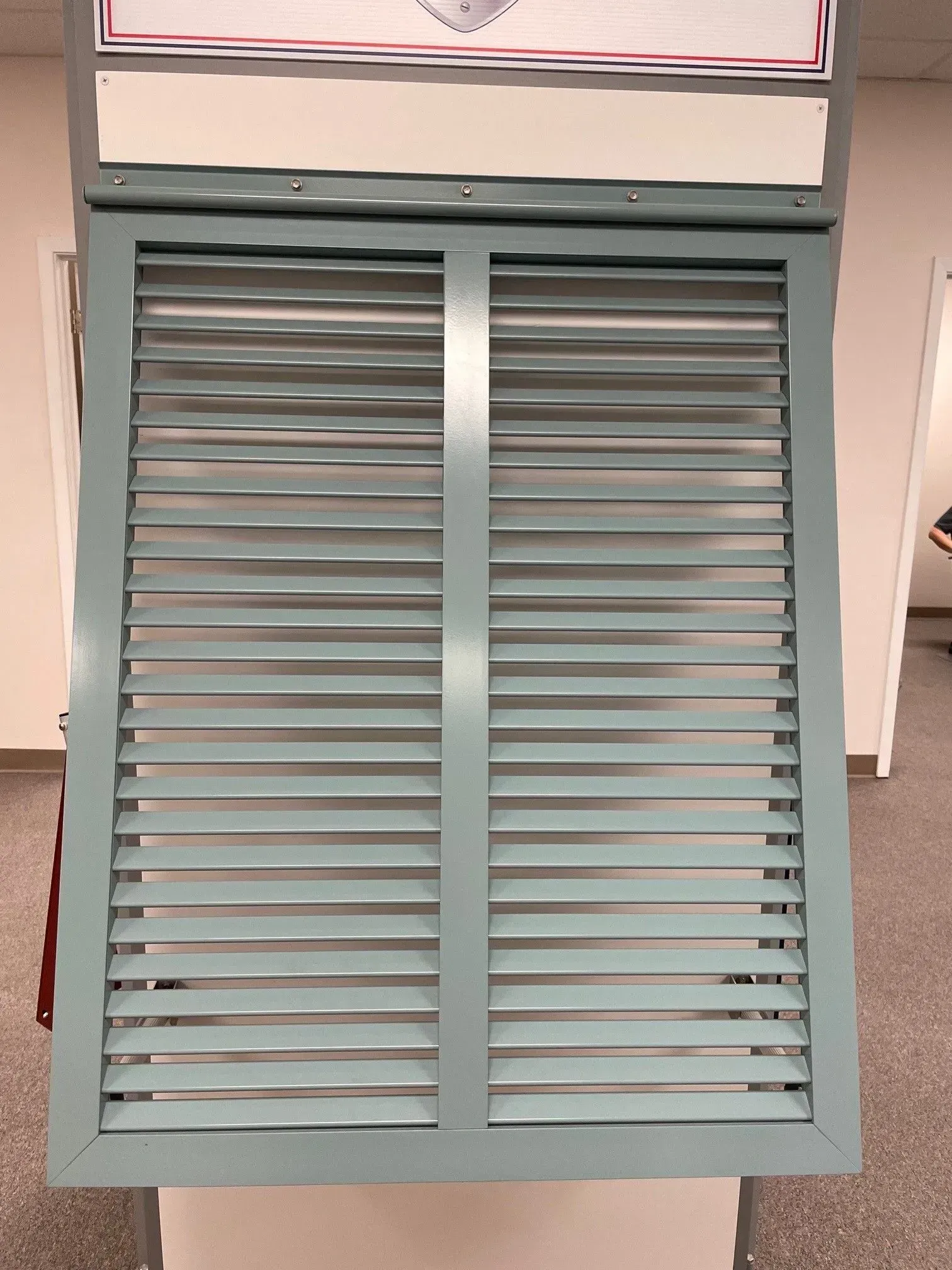 A light blue louvered shutter displayed on a stand.