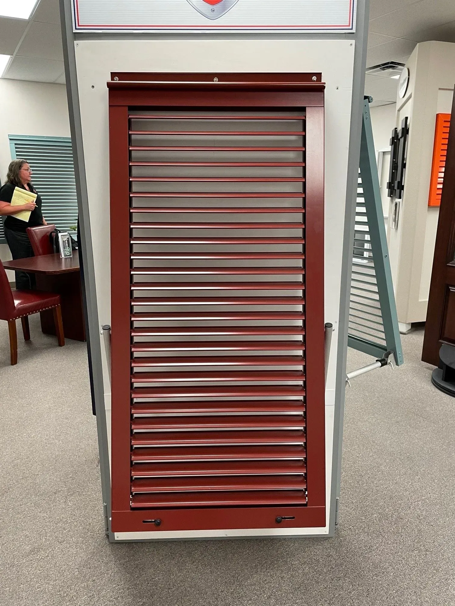 Red shutter display on a white wall in a store. A woman is partially visible in the background.