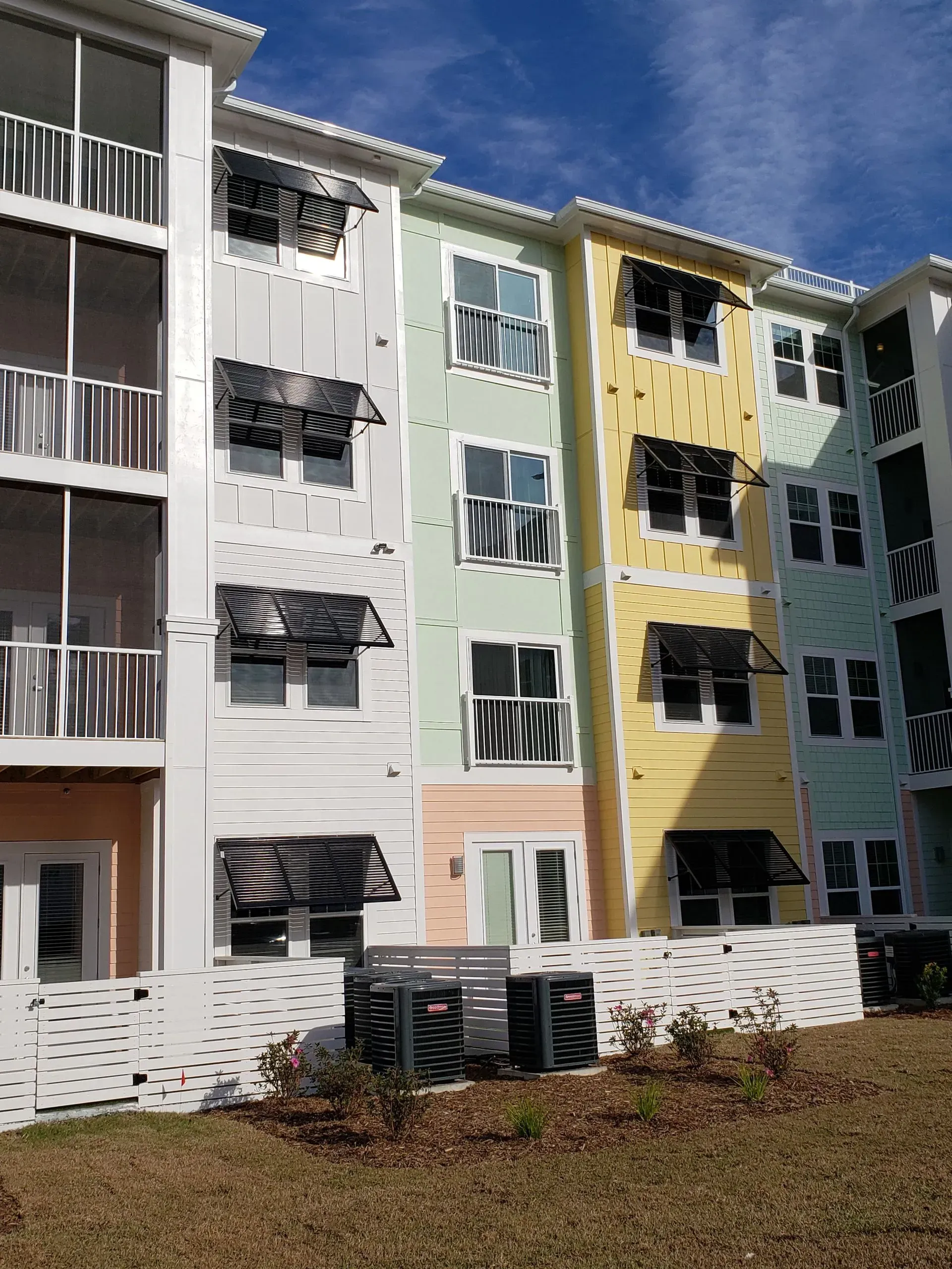 Multi-story apartment building with pastel-colored siding and black awnings.