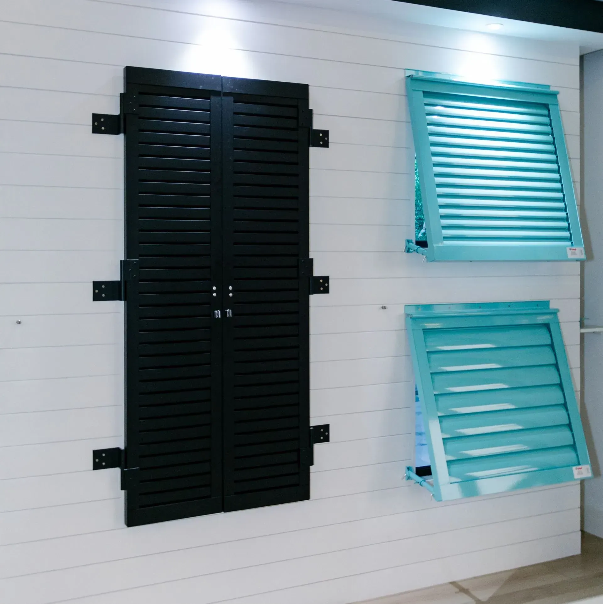 Black shutters, teal shutters, mounted on white horizontal plank wall.