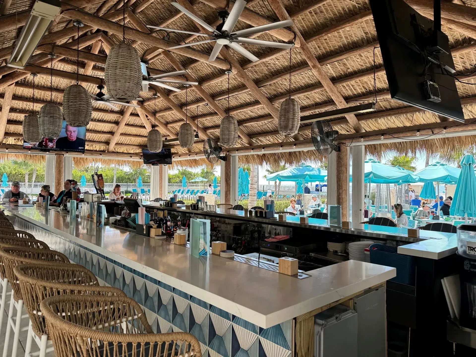 Beachside bar with thatched roof, stools, and open windows overlooking pool and ocean.