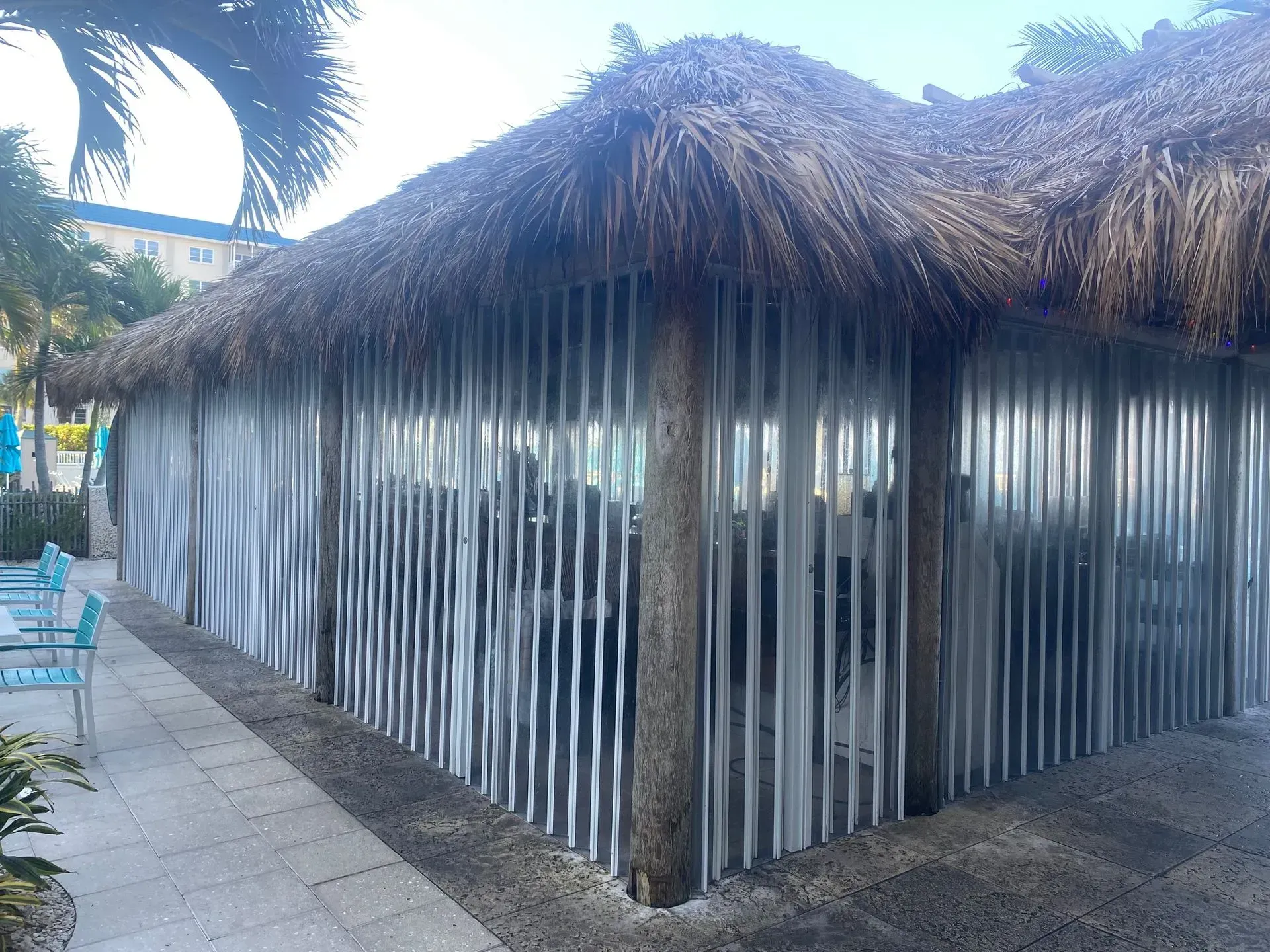 Tiki hut with corrugated metal walls, thatched roof, and concrete walkway.