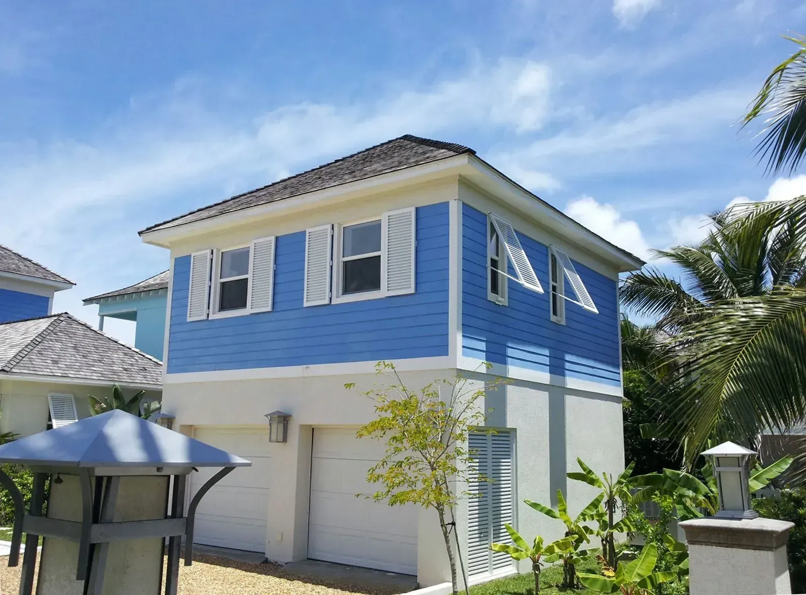 Two-story blue and white building with shutters and garage doors. Palm trees and blue sky background.