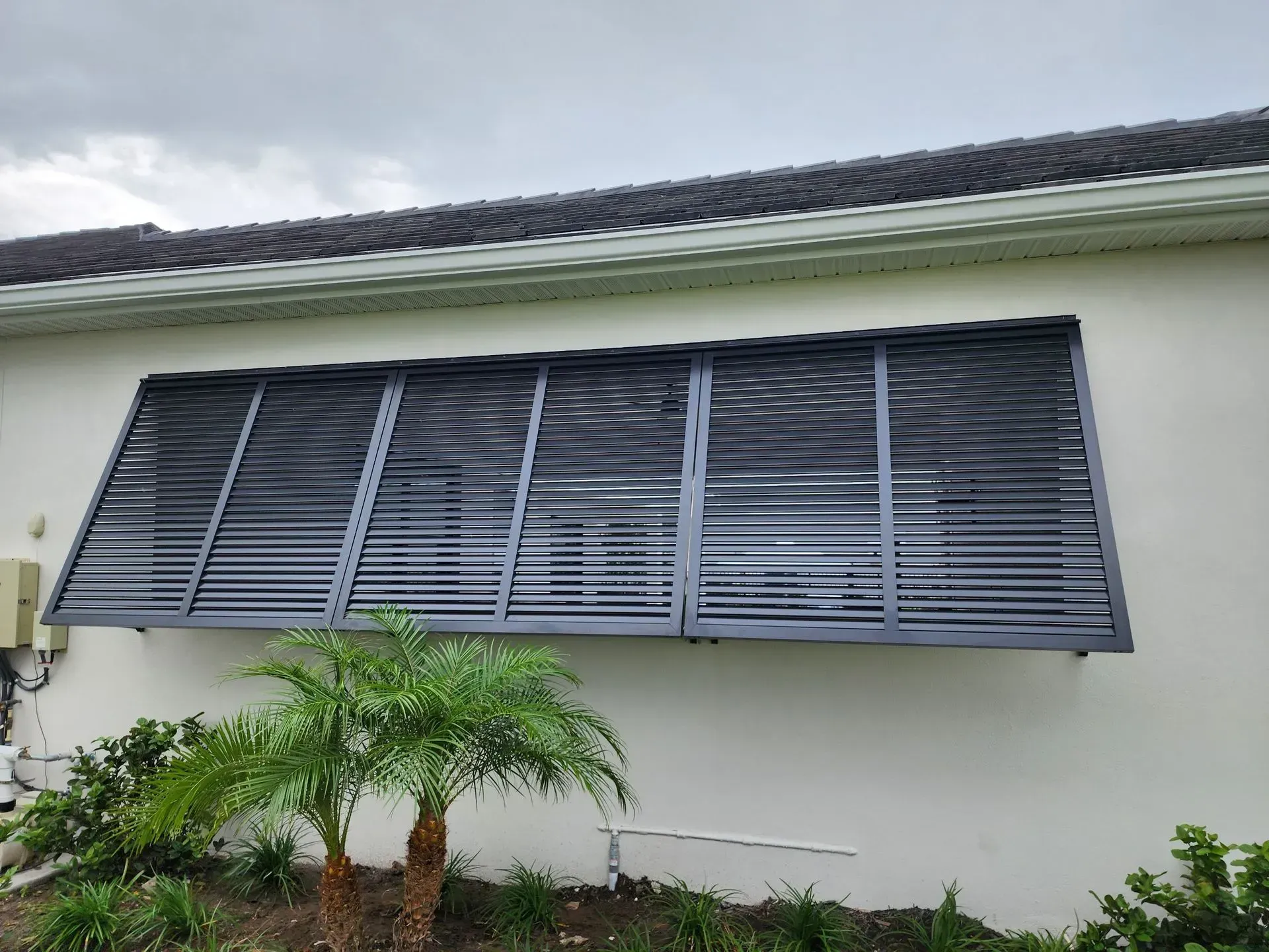 Exterior of a building with dark gray, slatted hurricane shutters over a window.