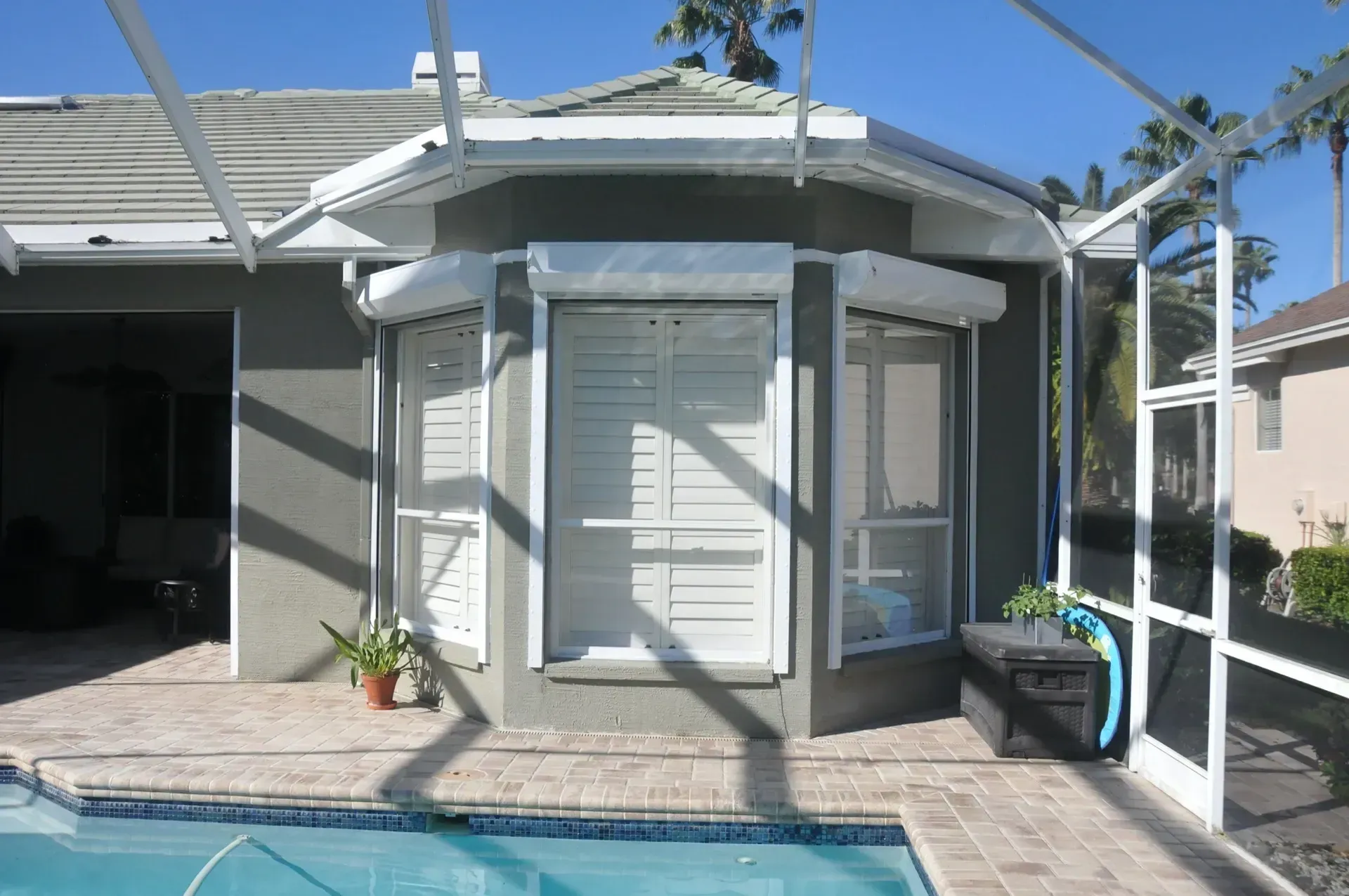 Exterior view of a house with white shutters on windows and a screened pool.