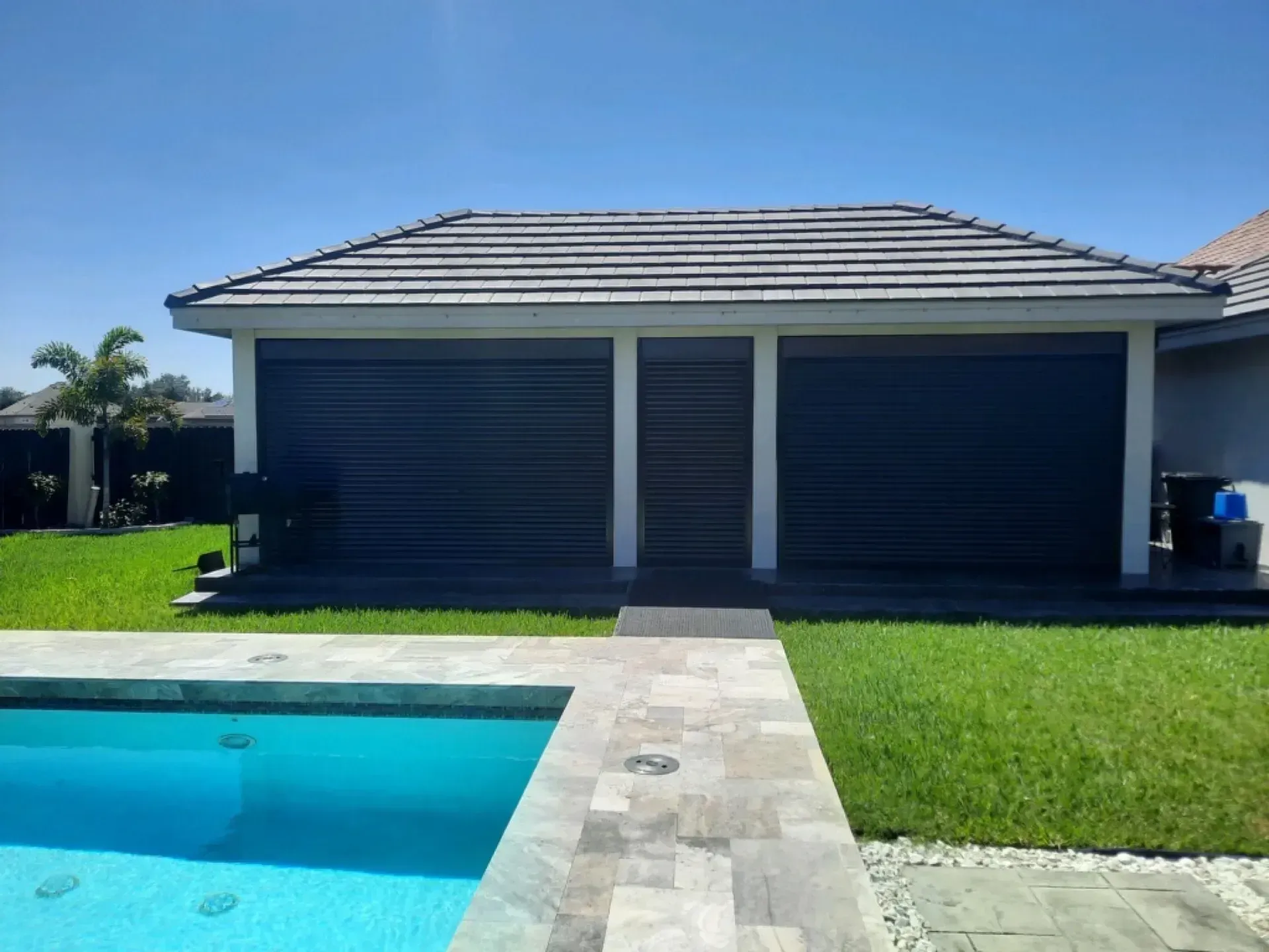 Poolside cabana with dark blue shutters, tile roof, and stone pathway leading from the pool.
