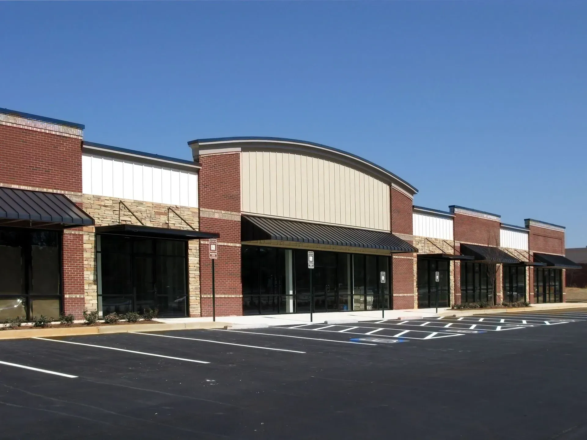 Storefront building with brick and stone accents, awnings, and a parking lot.