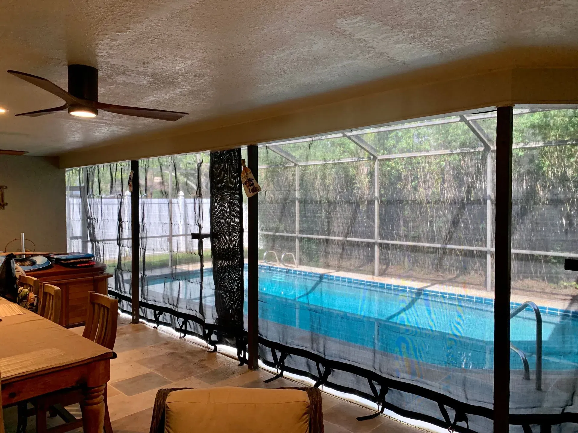 Enclosed pool patio with black mesh screens, a blue pool, and a ceiling fan.