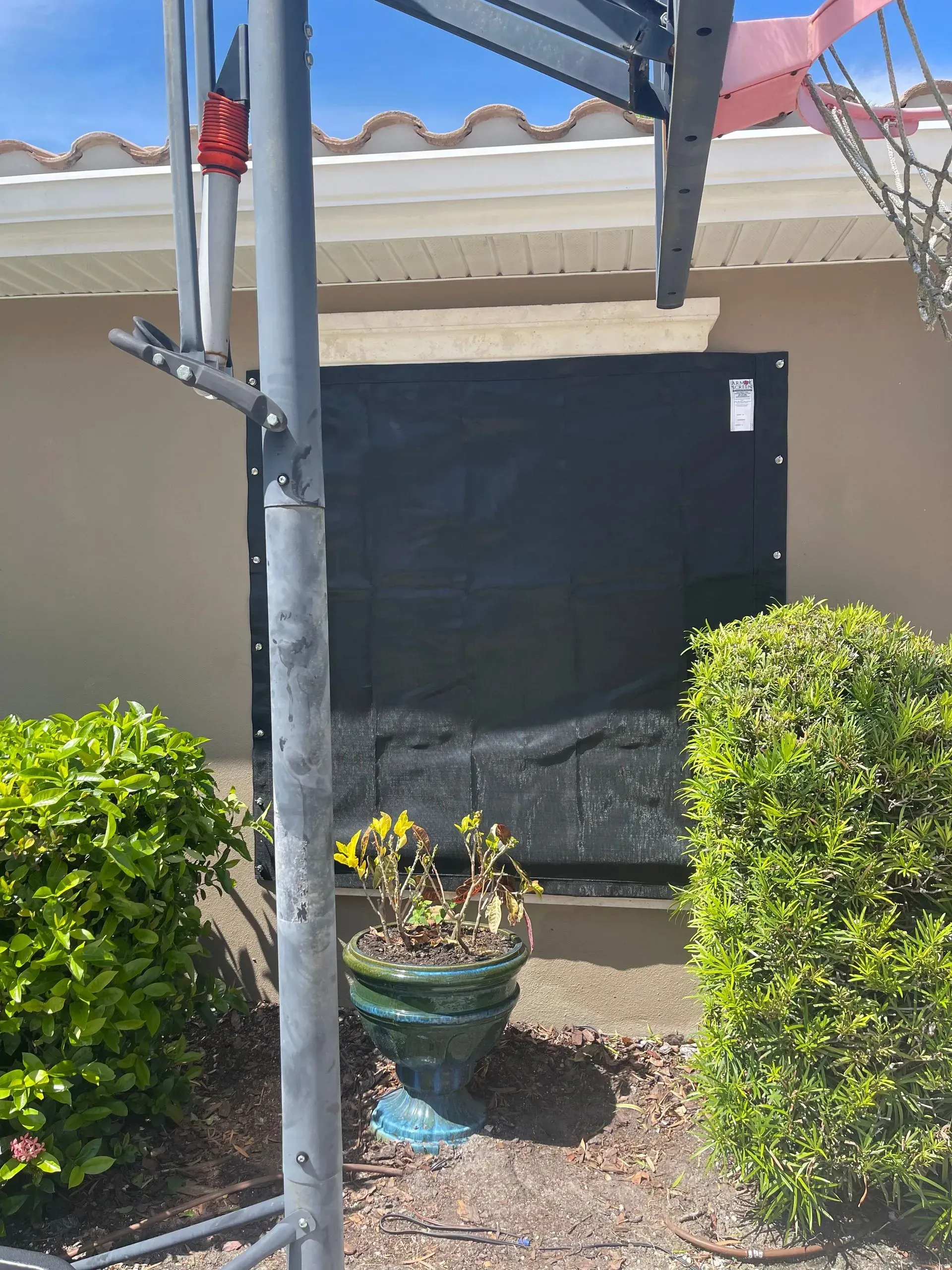Black tarp covering a doorway on a tan house exterior, next to a basketball hoop pole and bushes.