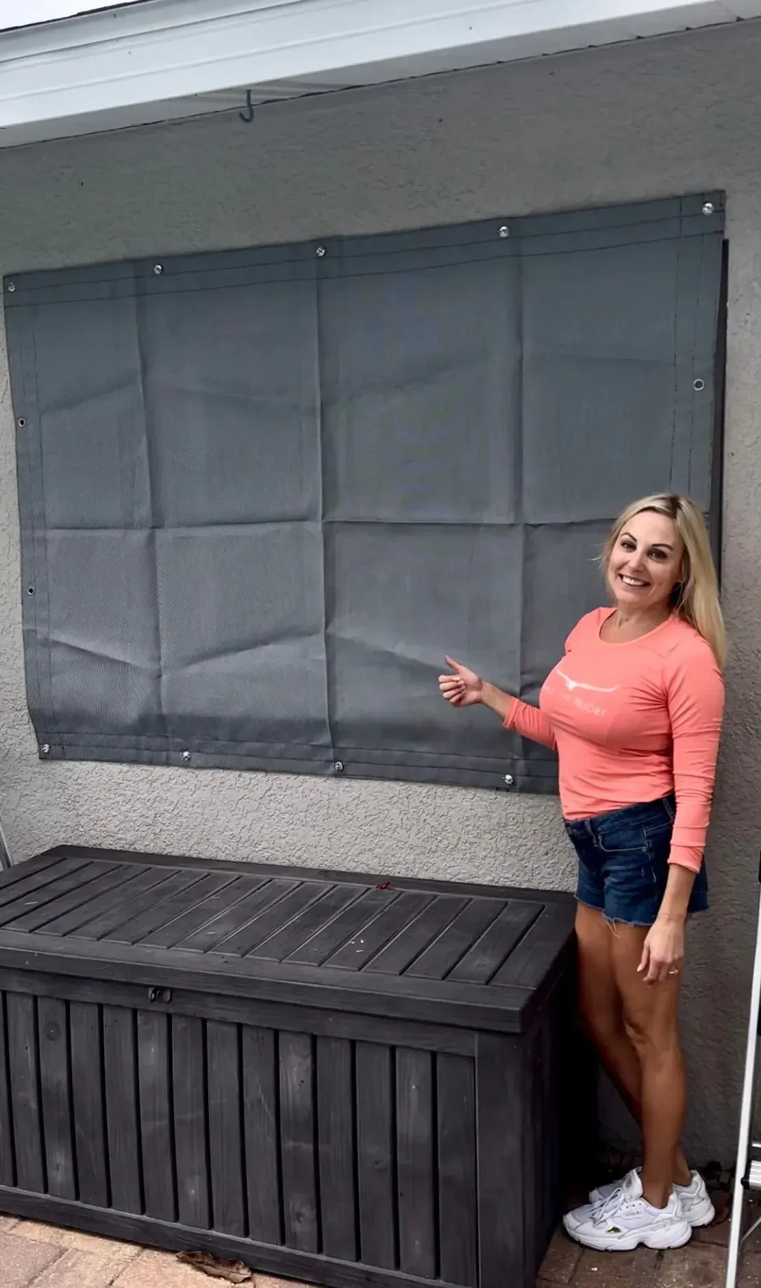 Woman points to a gray sunshade on a wall above a black storage chest.