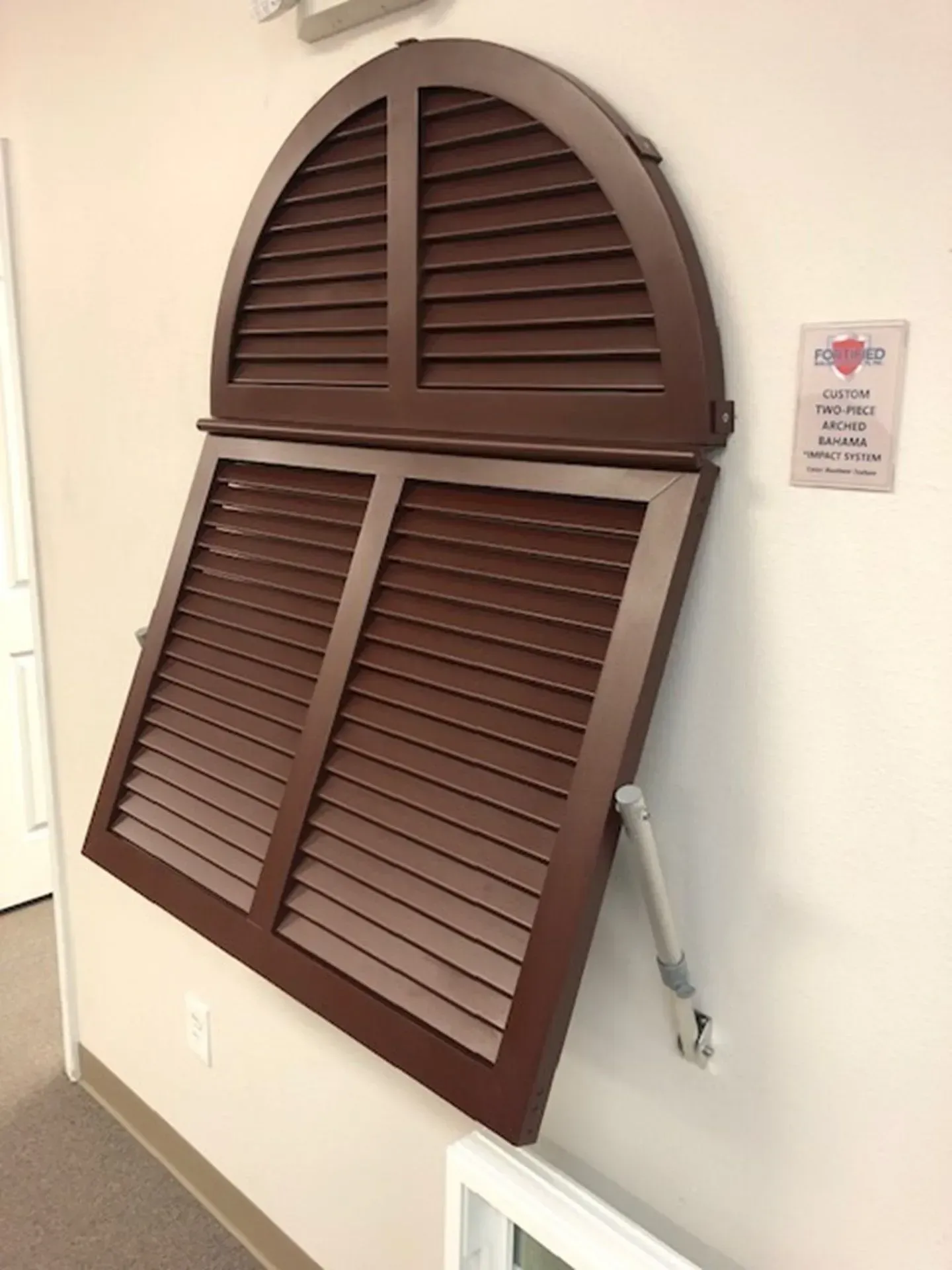Brown shutter window display on white wall, with arched top, tilted open.