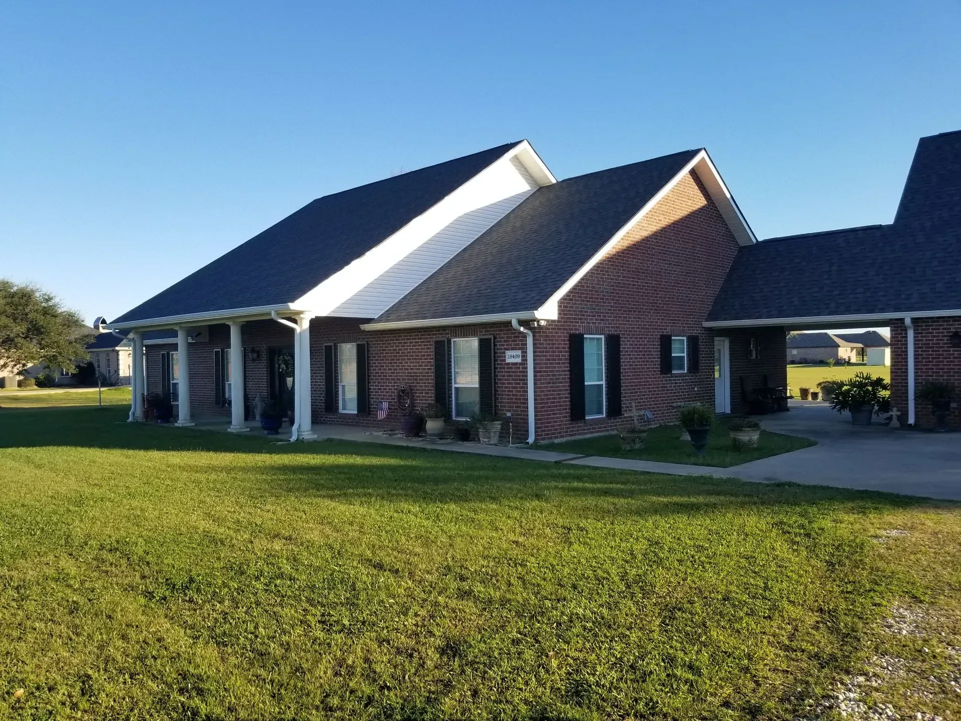 Brick house with black roof, white trim, and a covered entrance. Green grass and clear sky.