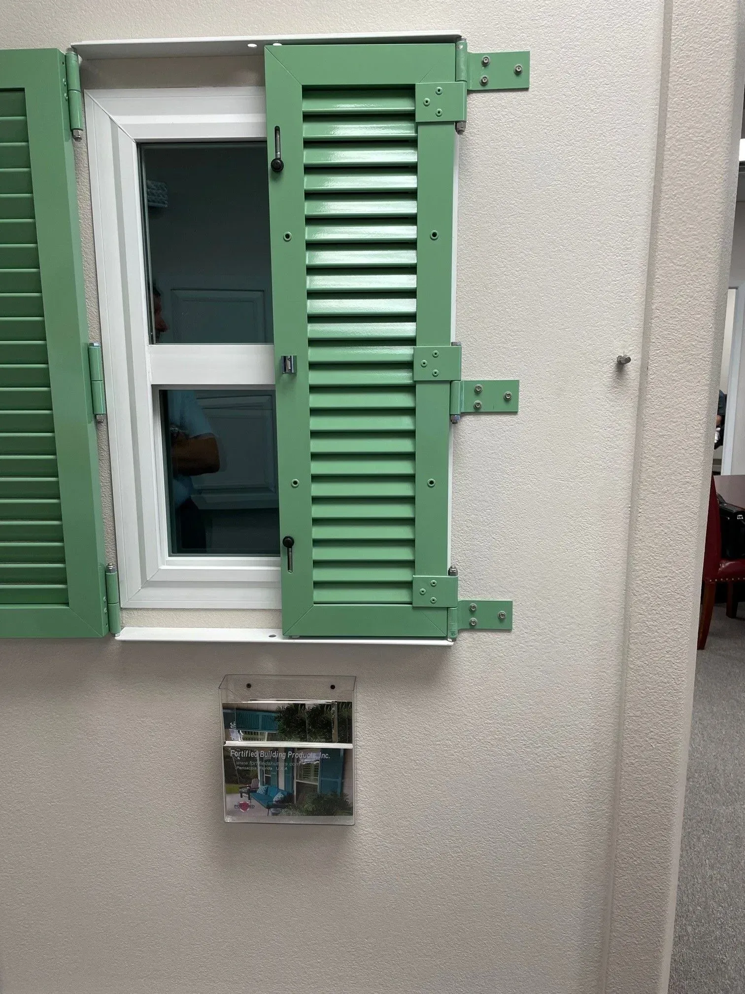 Green shuttered window on a light stucco wall, open to the left, with a small metal box below.