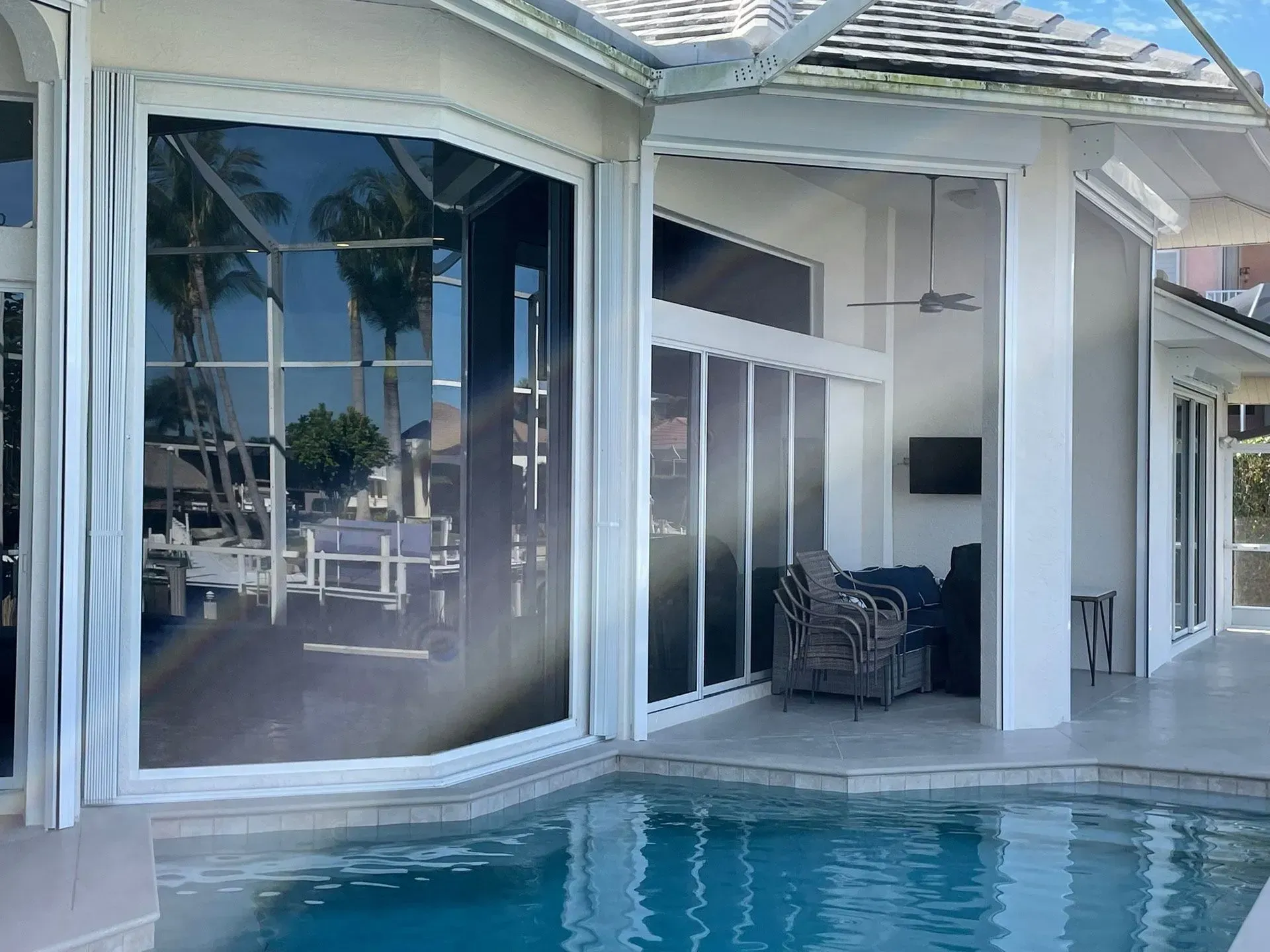 Poolside view of a white house with large windows, reflected in the pool water.