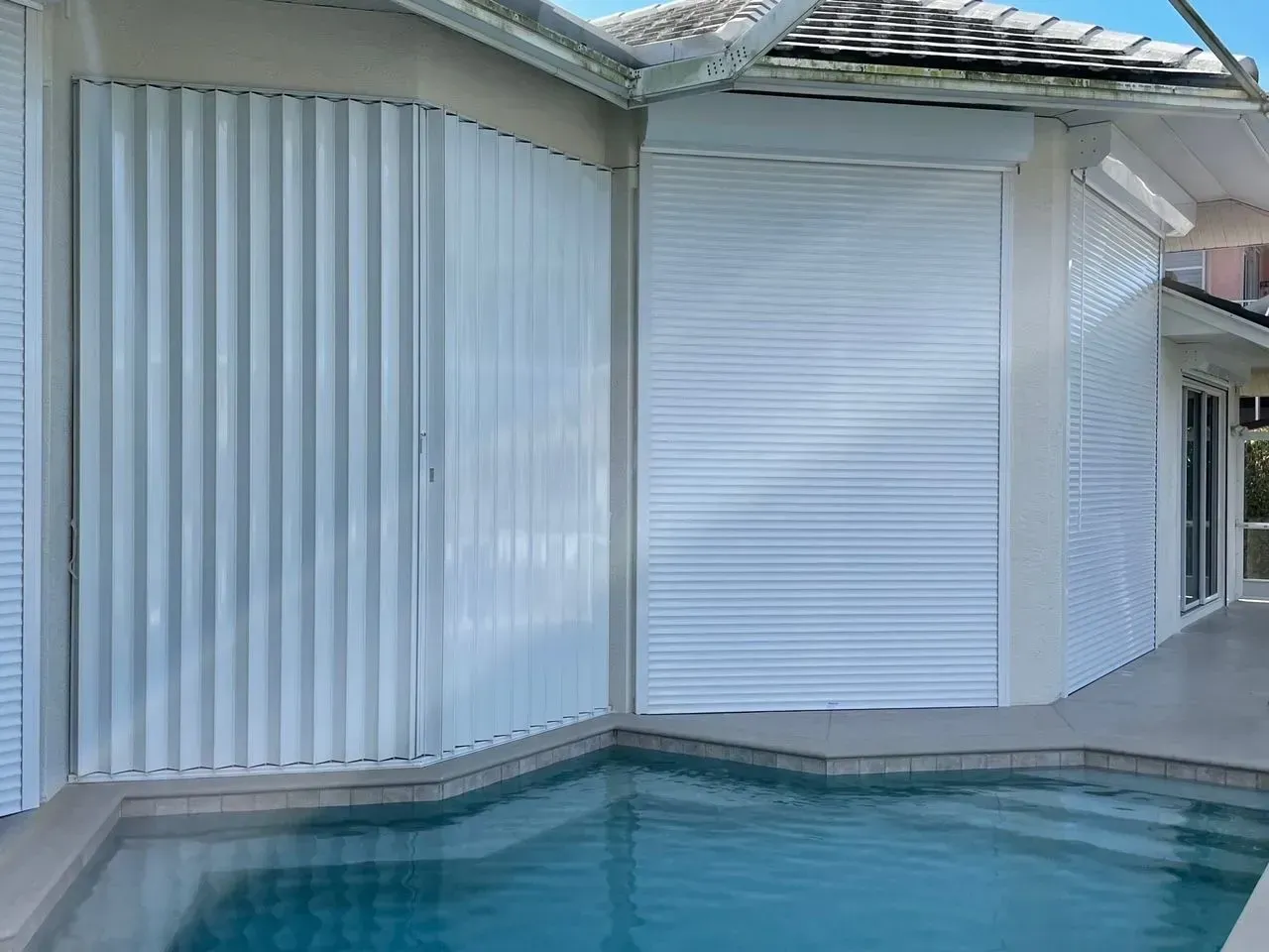 White hurricane shutters cover the exterior of a house by a pool.