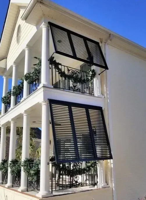 Two-story white house with balconies. Black shutters are open above the balconies. Green garland decorates the railings.