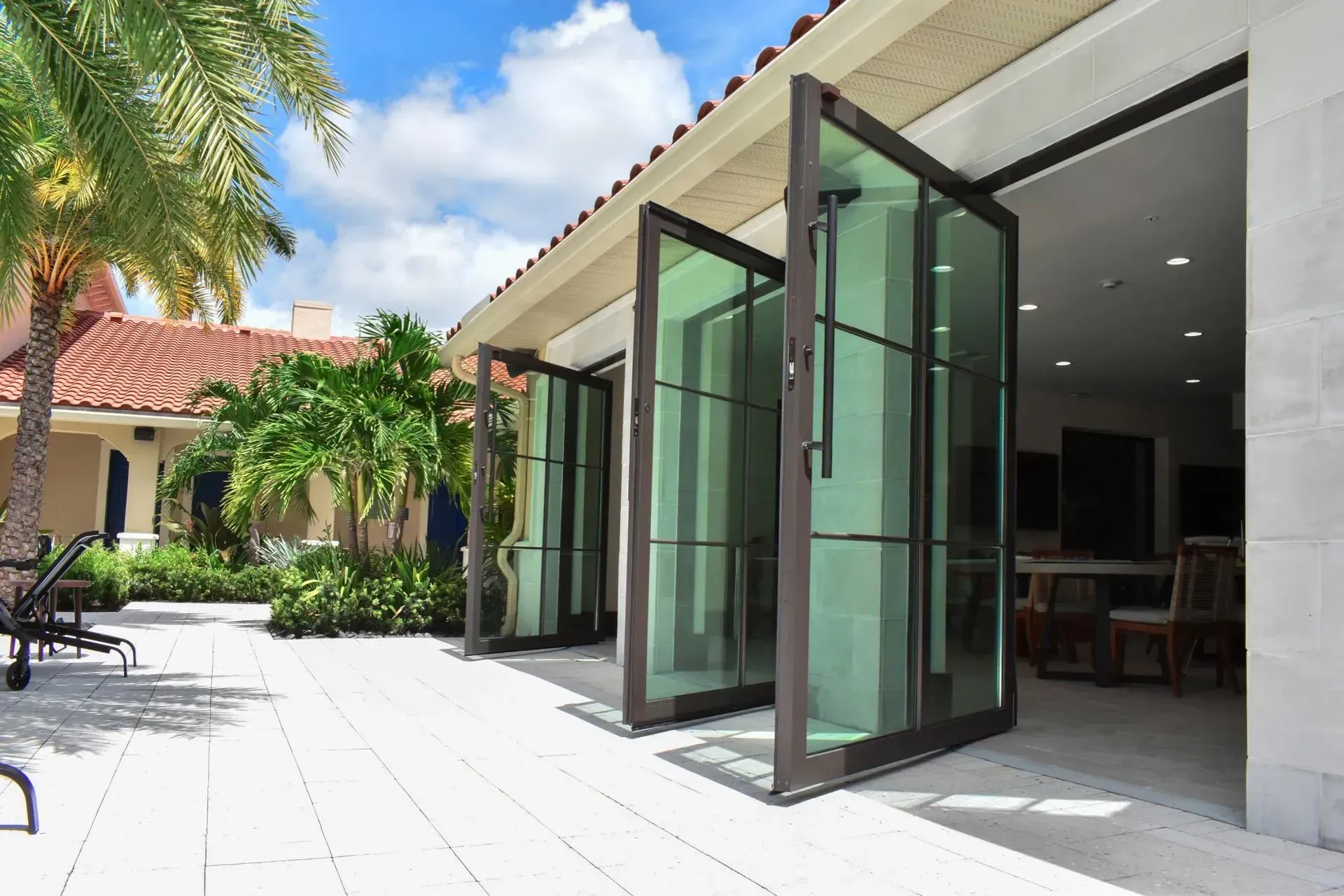 Exterior view of a house with open, folding glass doors overlooking a patio with palm trees.