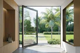 Glass door open to a lush backyard with palm trees and a square window on the side.