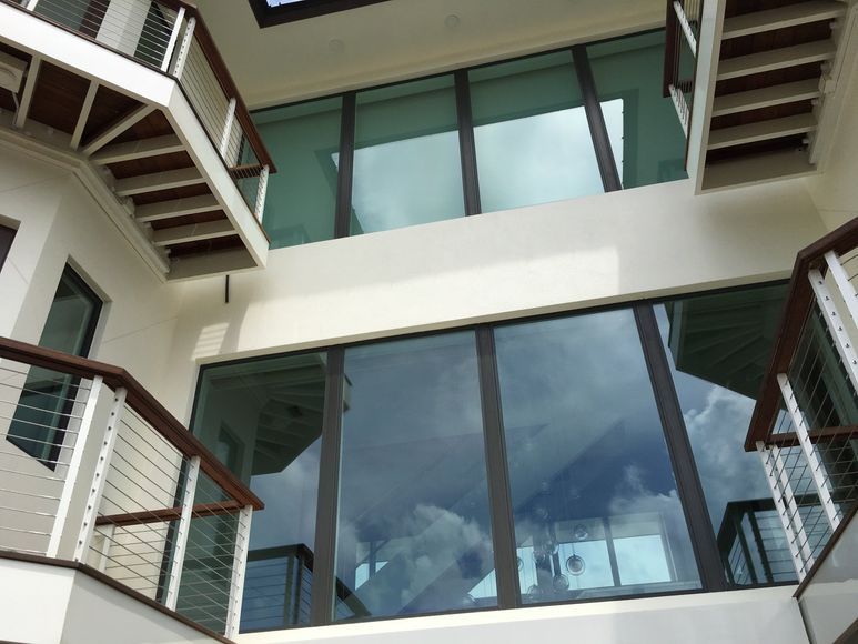 Interior atrium with large windows reflecting the sky, flanked by balconies with wooden rails and steel cables.