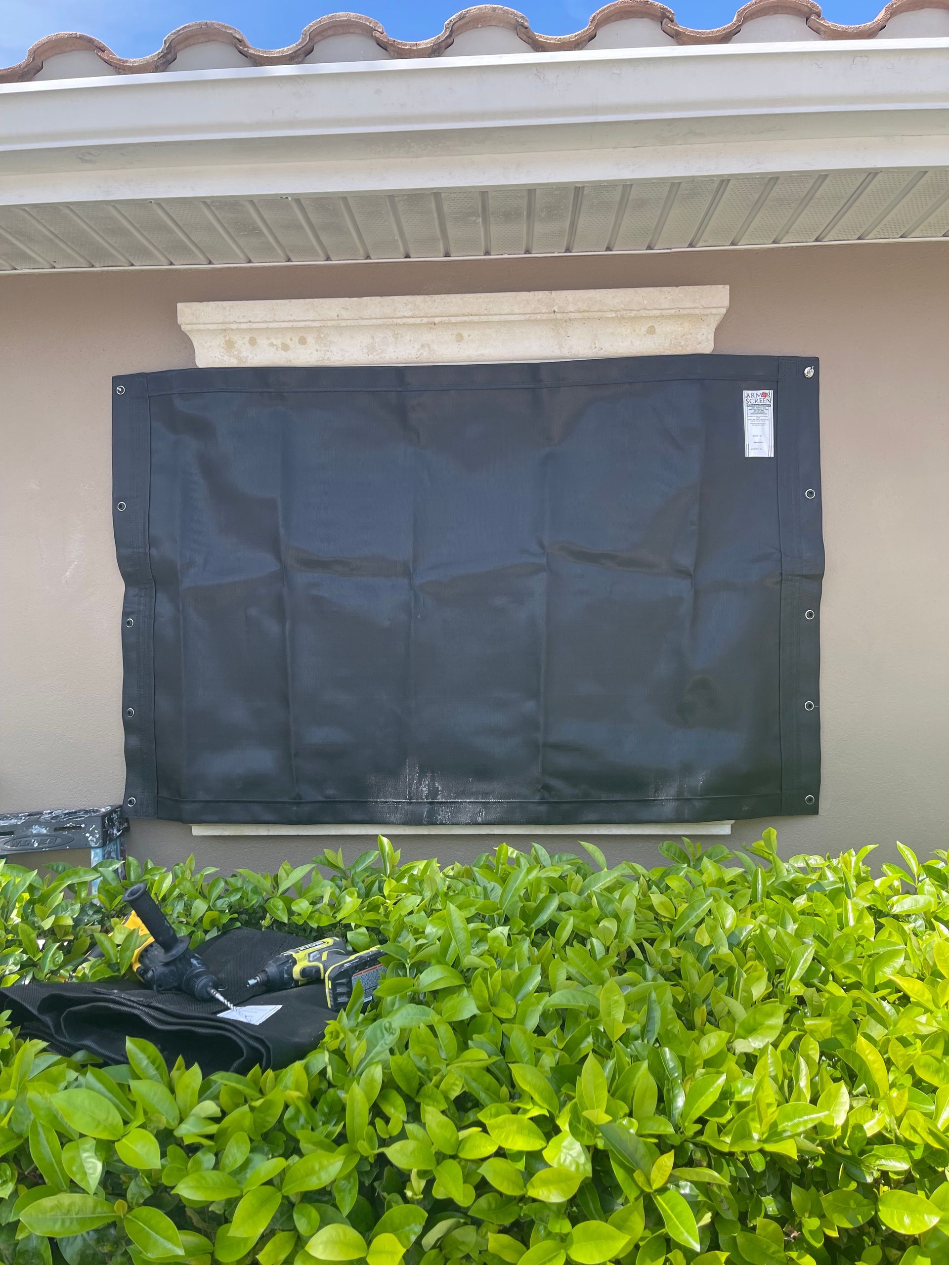 Black fabric storm shutter covering a window on a beige stucco wall, outdoors.