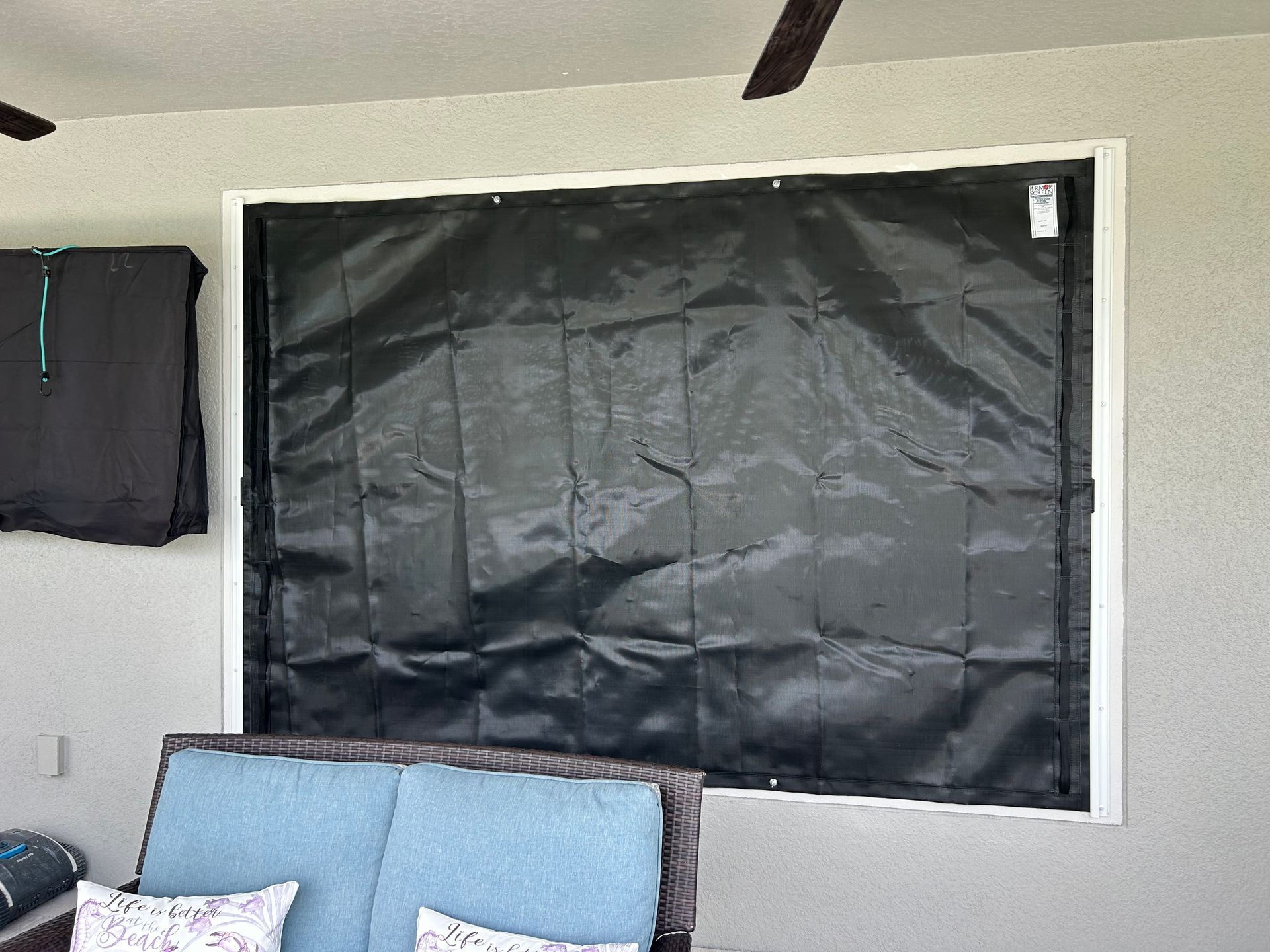 Black fabric covering a window frame on an outdoor wall. A blue cushion and a black shirt are visible.
