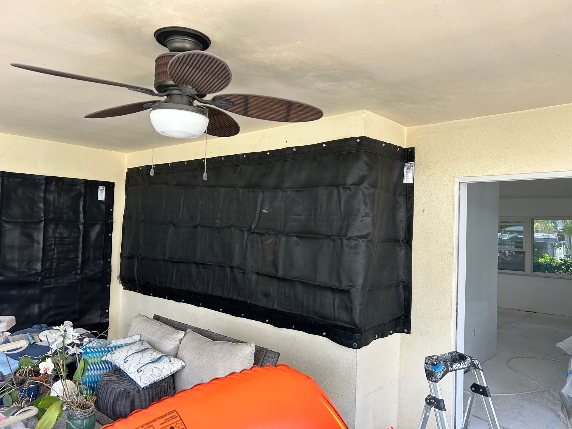 Outdoor space with black fabric covering windows; ceiling fan.