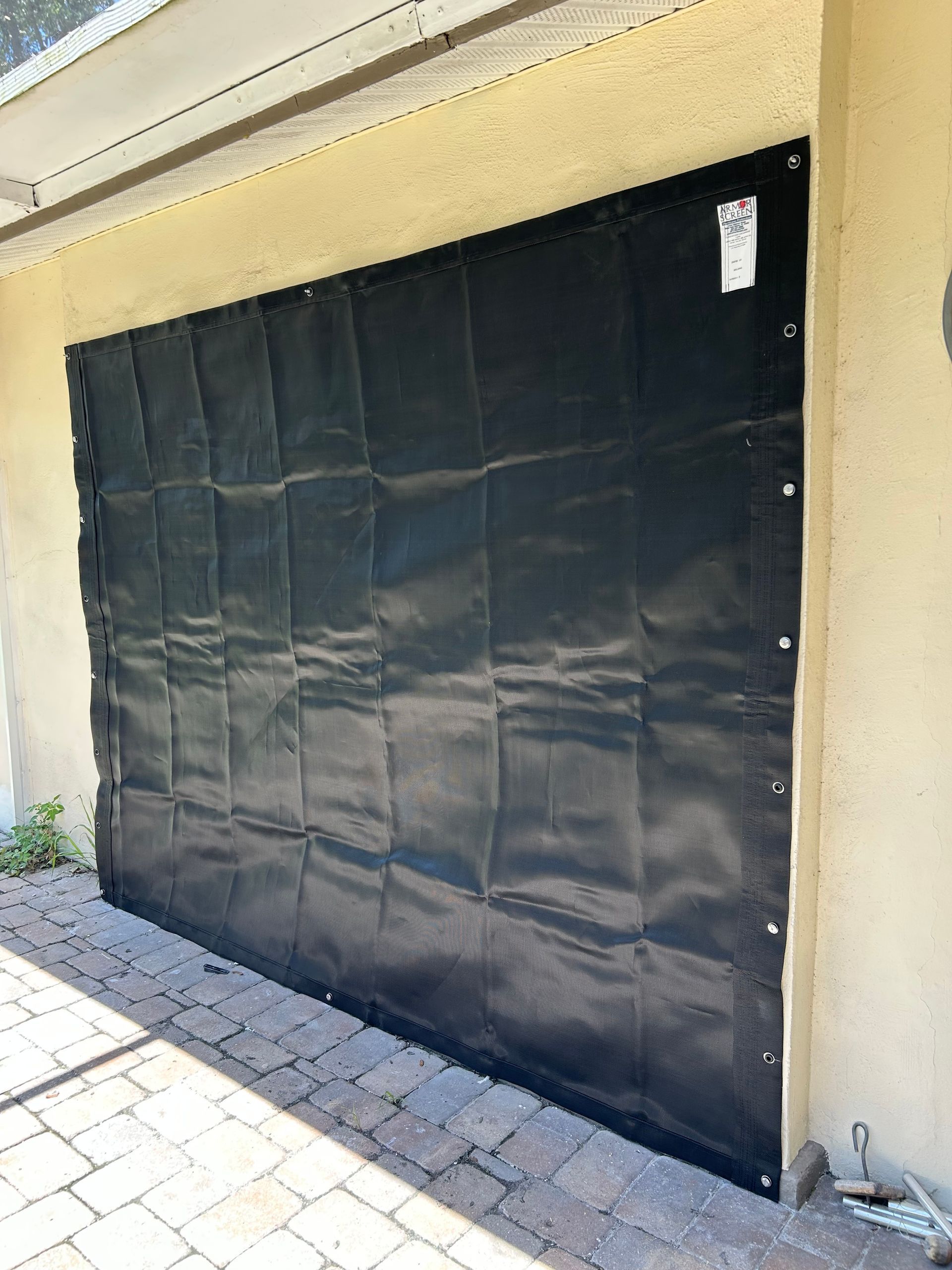 Black tarp covering a garage door opening, attached to the wall with rivets.