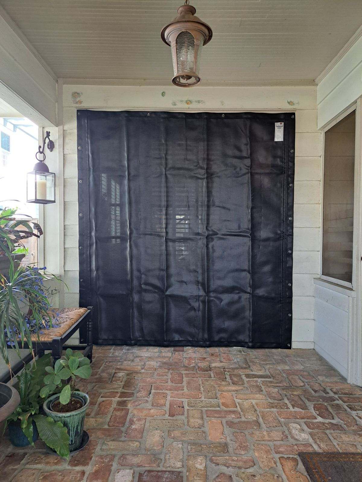 Black tarp covering a doorway on a brick-floored porch, under a hanging light.