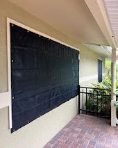 Black storm shutter on a beige house, next to a porch with a brick floor.