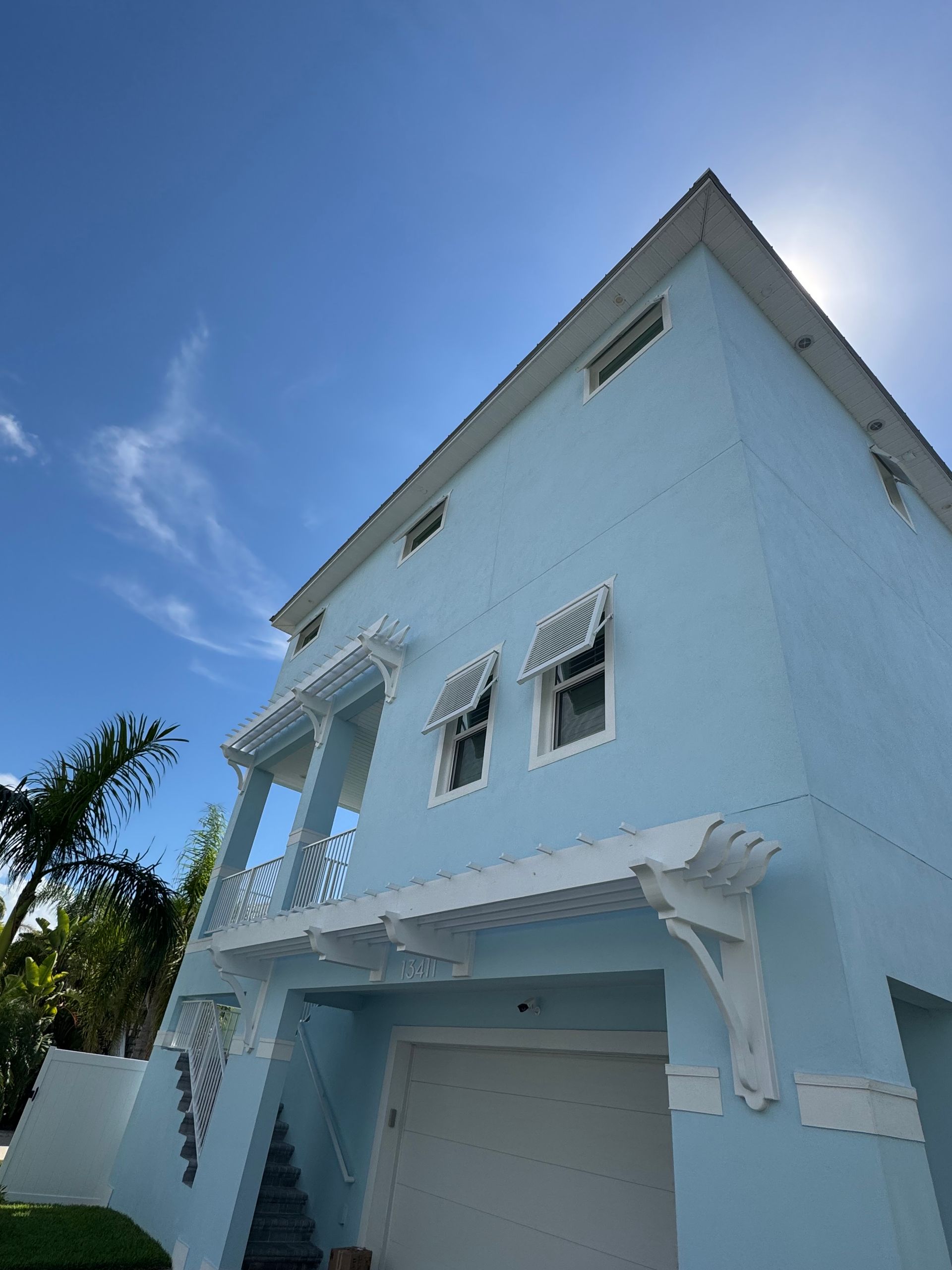 Light blue, multi-story house with white trim against a sunny, blue sky.