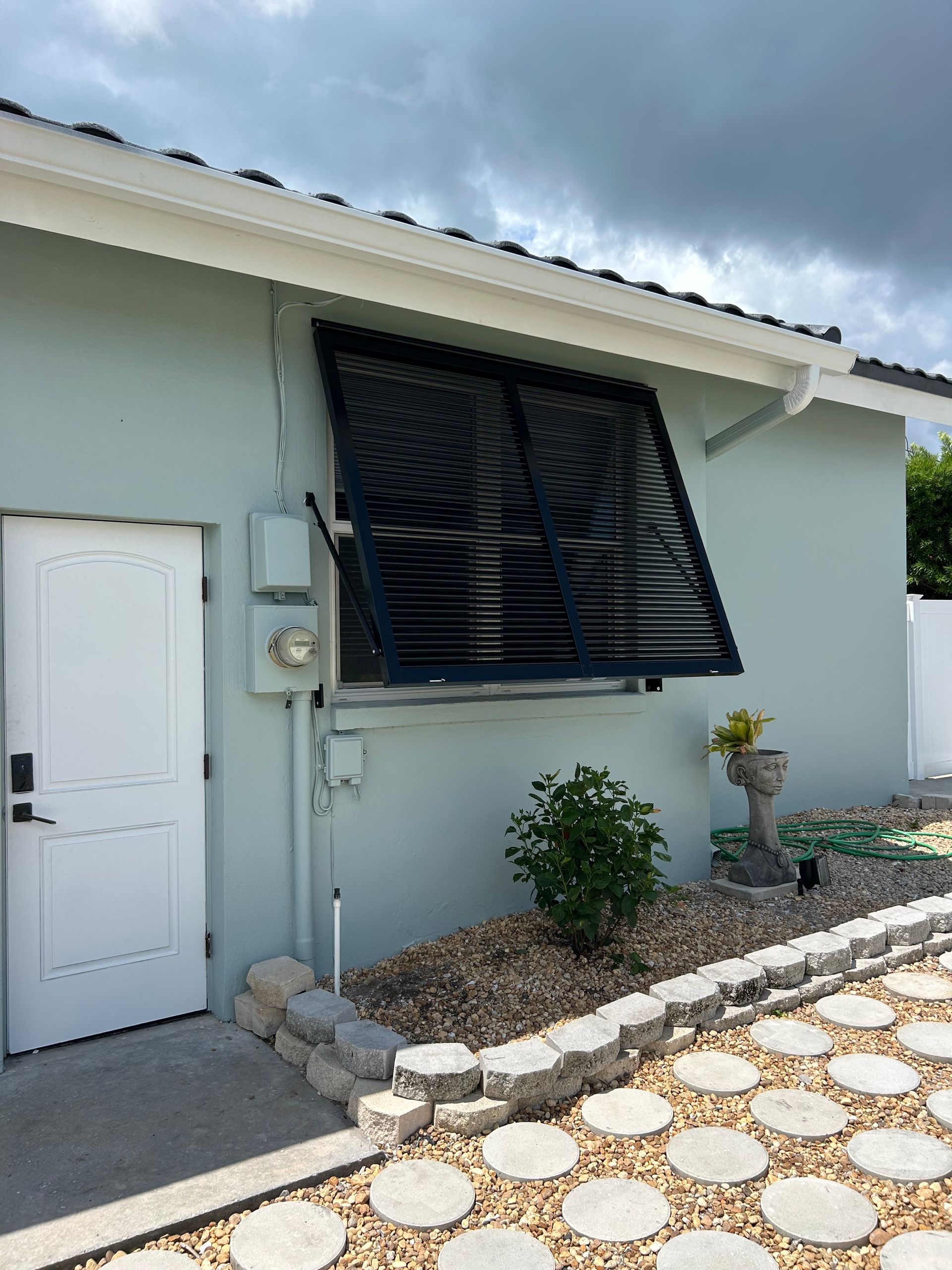 Light blue building with a white door, solar water heater, and small garden.
