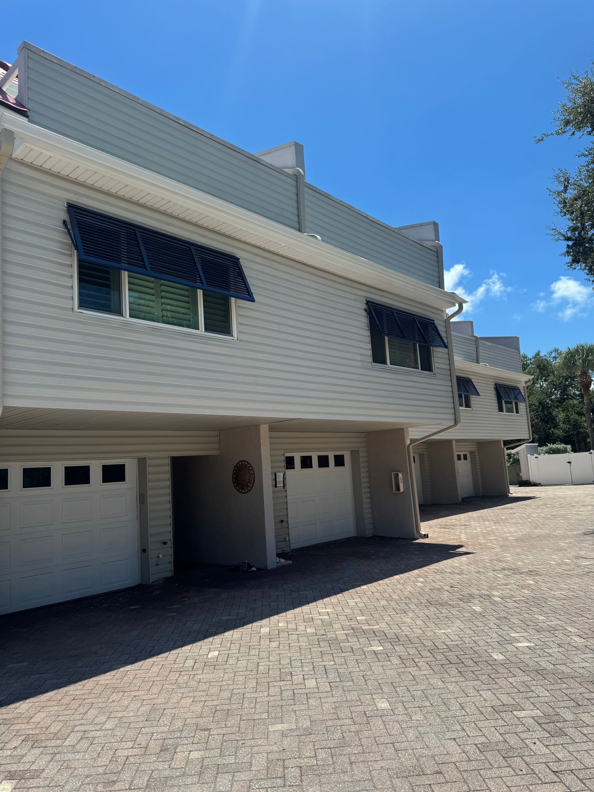 Row of white townhouses with garages. Blue awnings over windows. Sunny day.