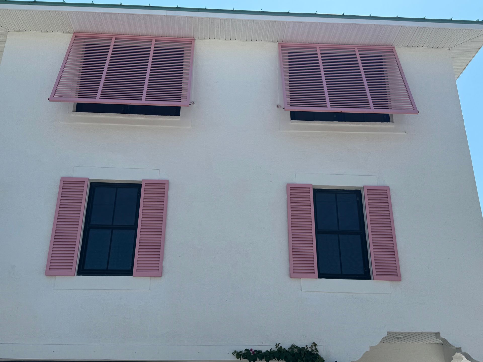 White building with pink shutters, two above and two below; blue sky in the background.