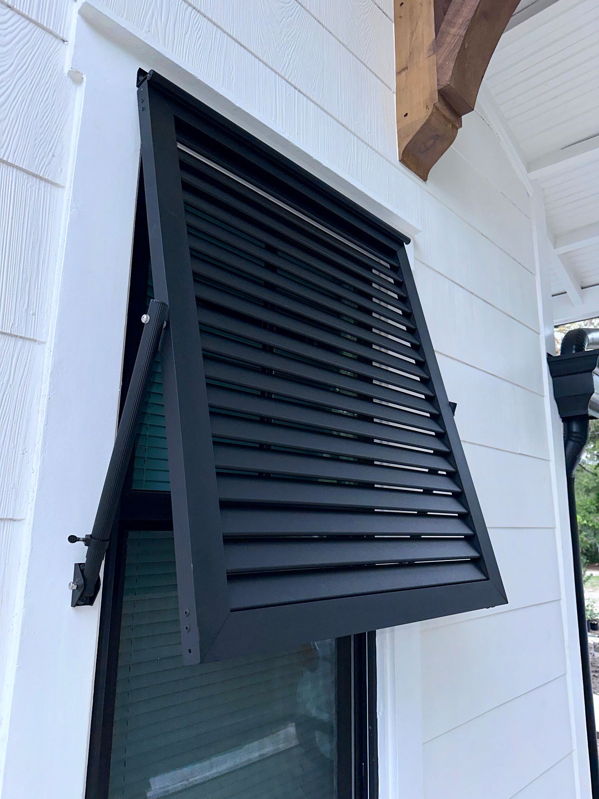 Black louvered shutter, open, over a window on a white house exterior.