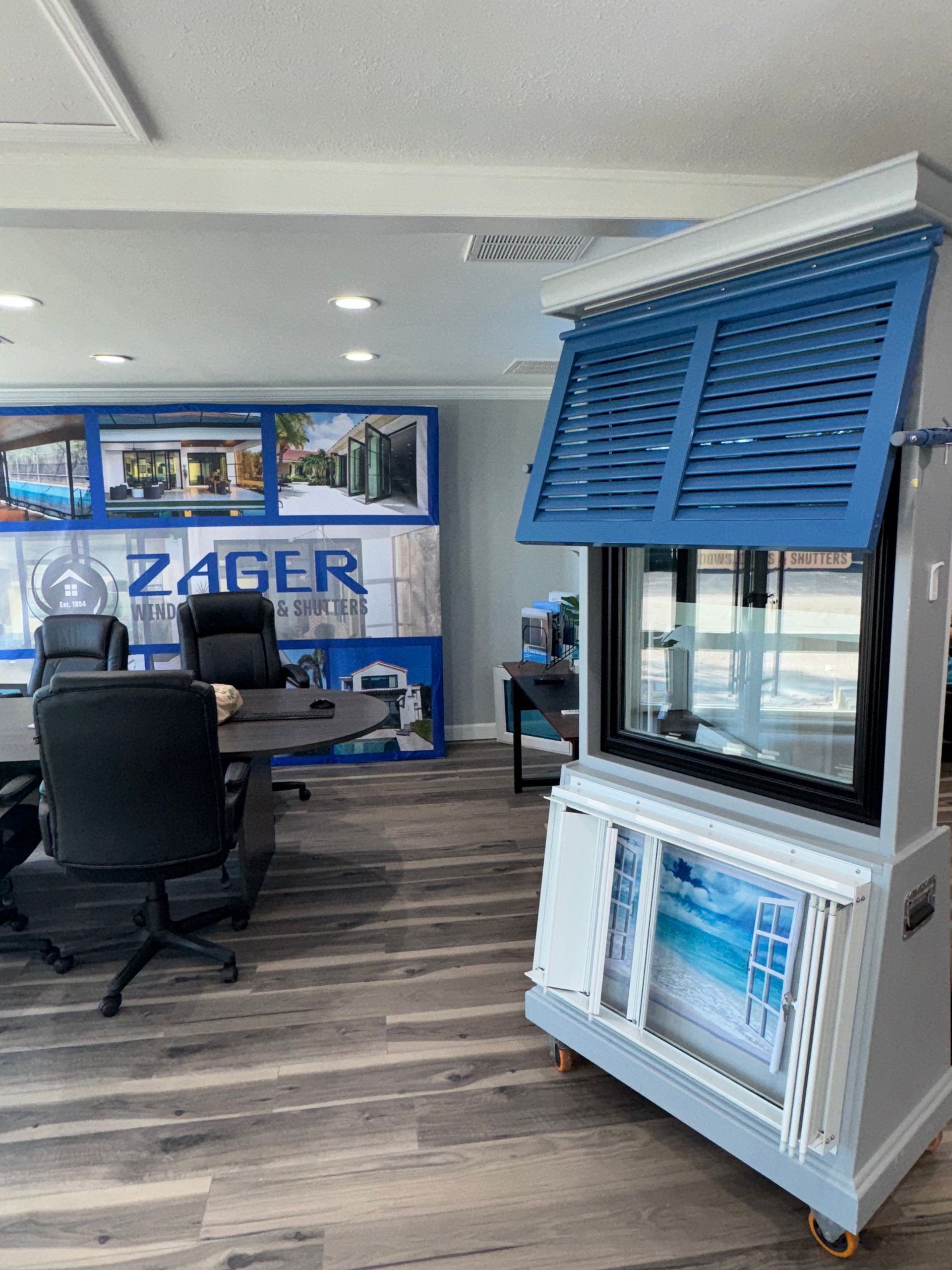 Interior shot of a showroom with window shutters display; blue shutters, wooden floor, and office setting.