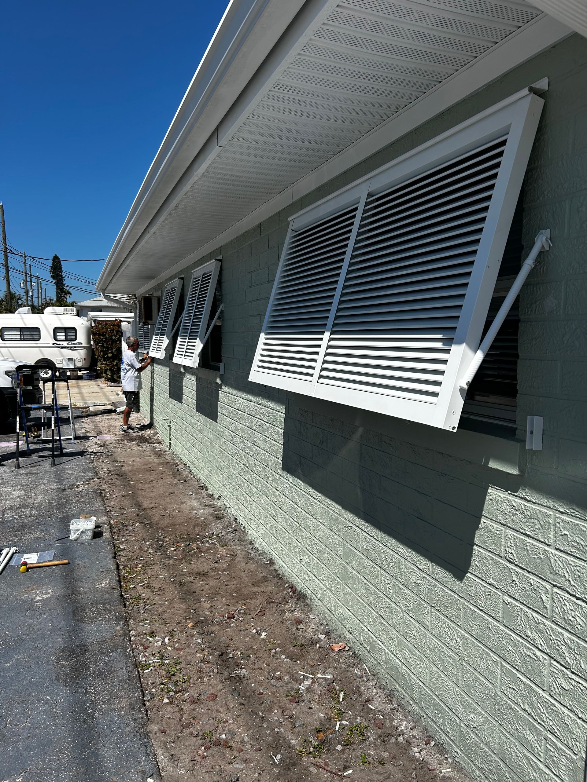White louvered window open on a light green building. Sunny day.