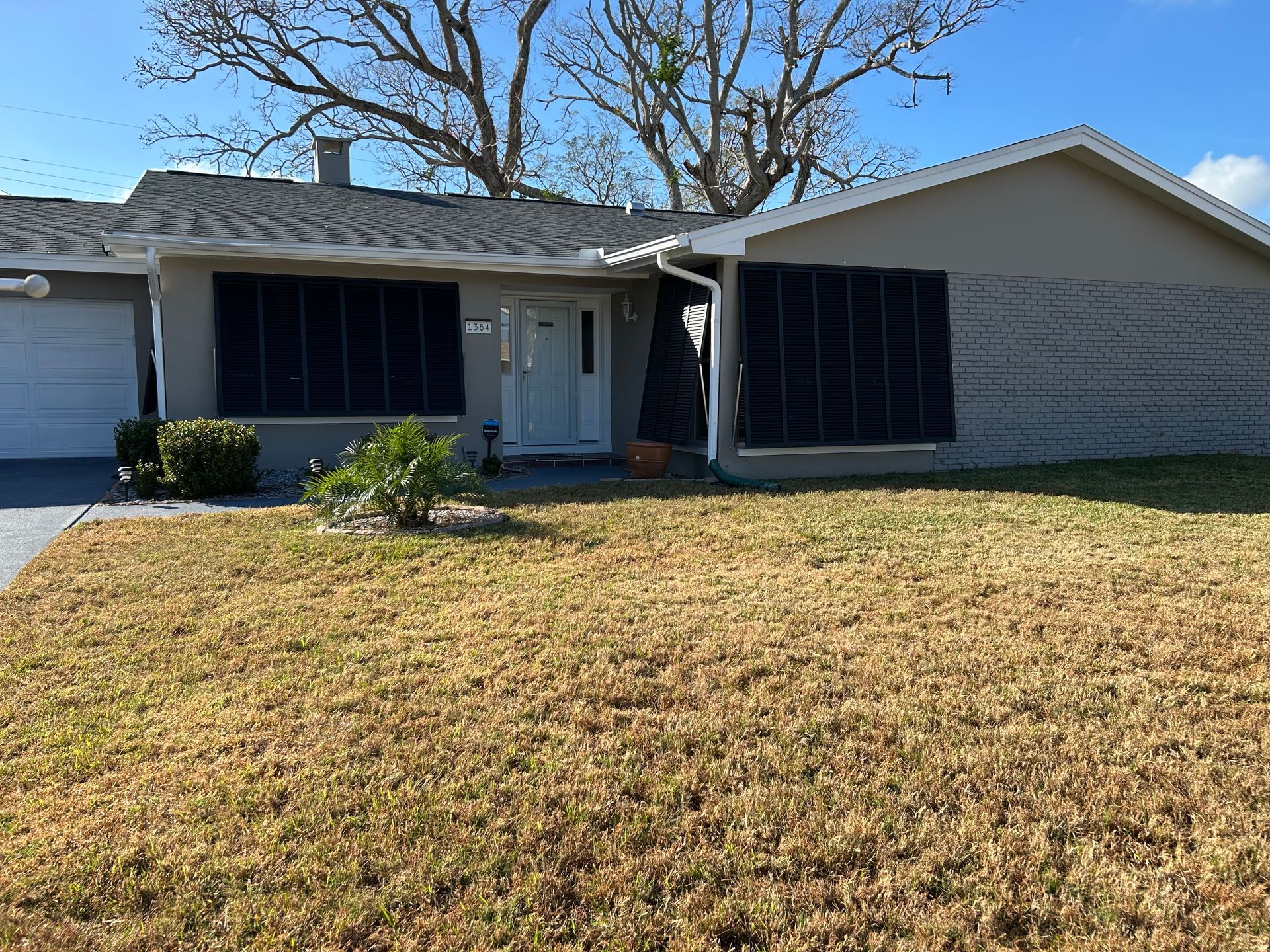 House with windows covered in dark screens, brown lawn, and blue sky.