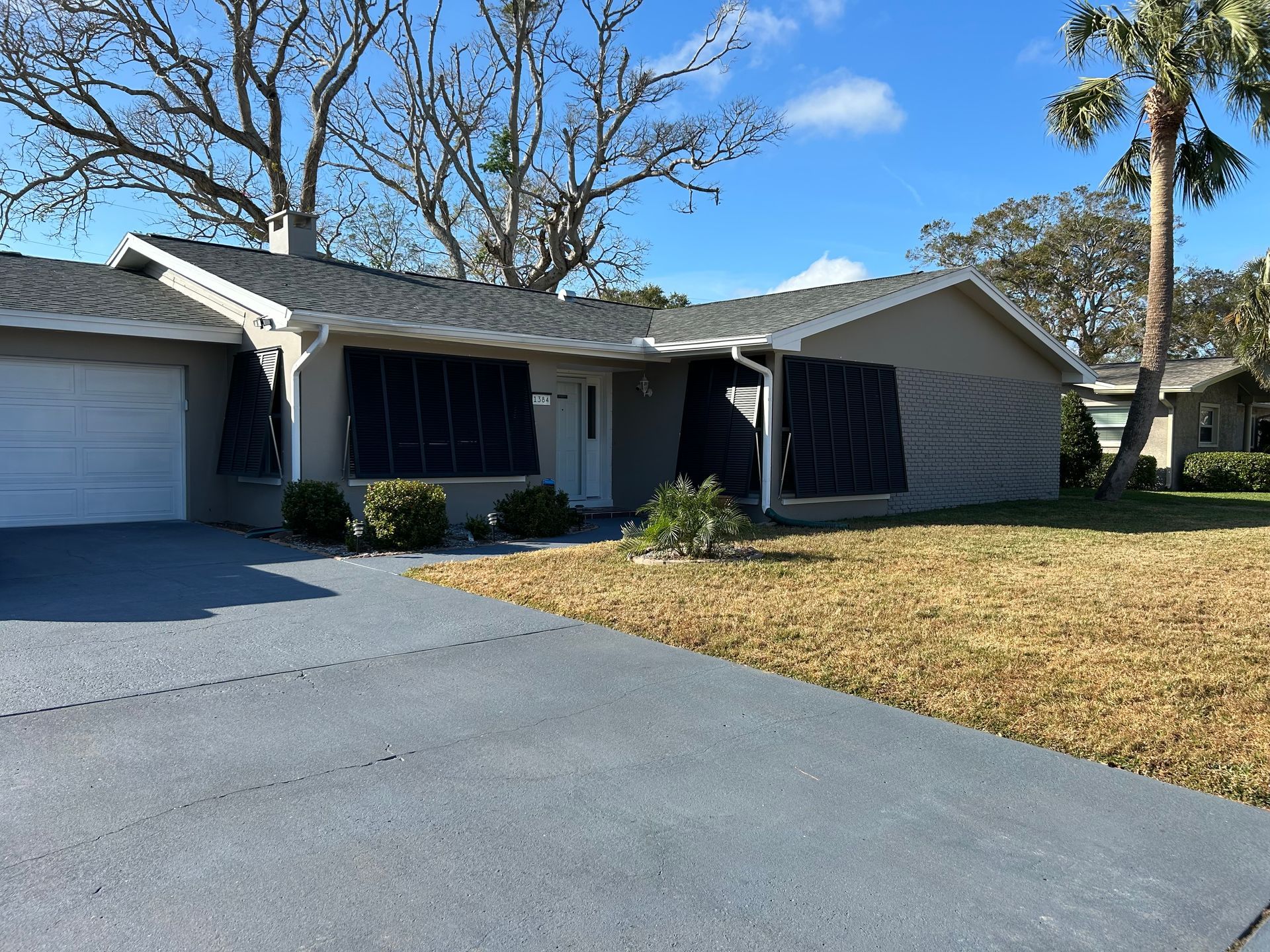 A light-colored house with solar panels on the windows and a blue driveway on a sunny day.