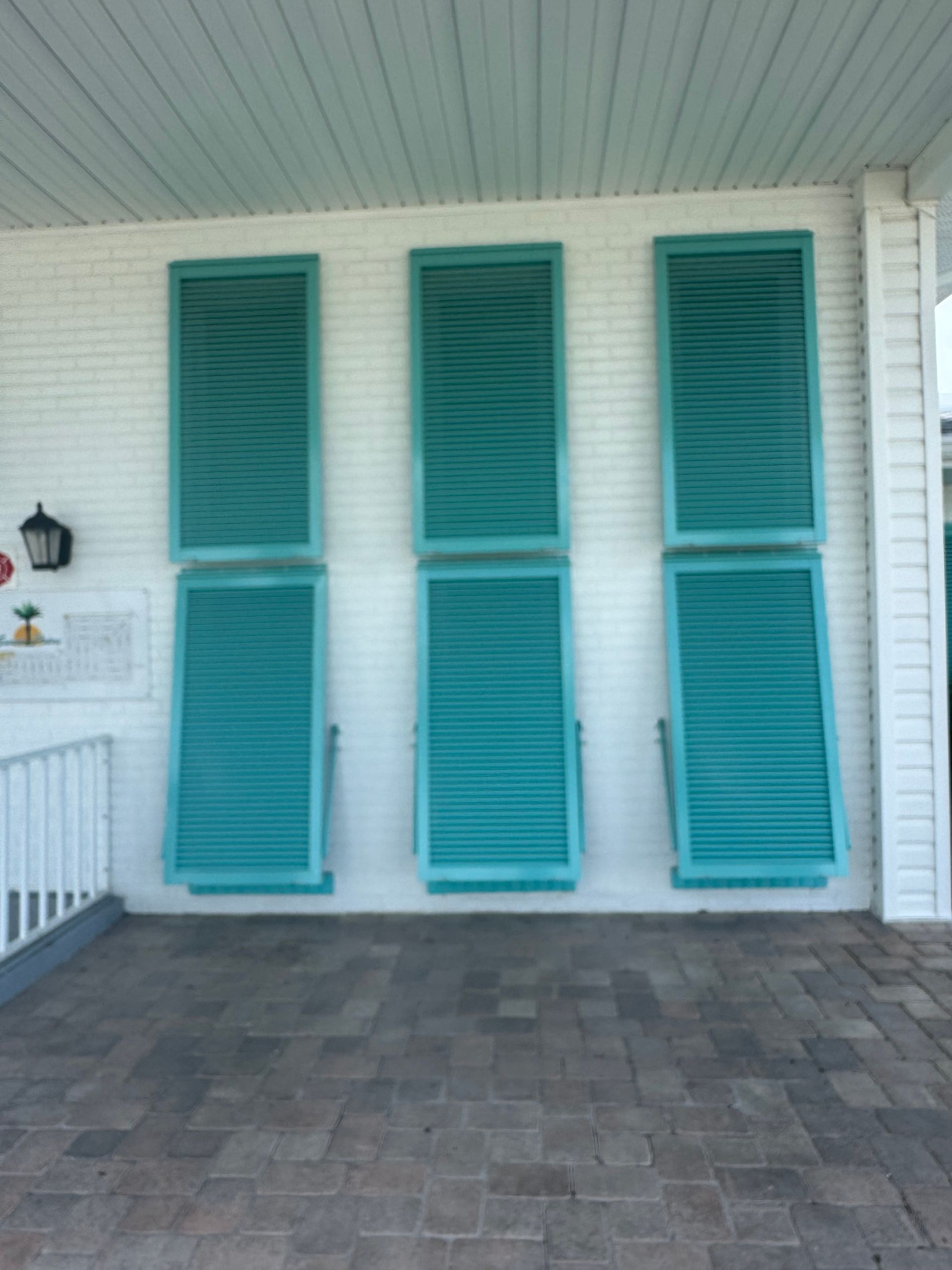 Three teal shutters attached to a white brick wall on a porch.
