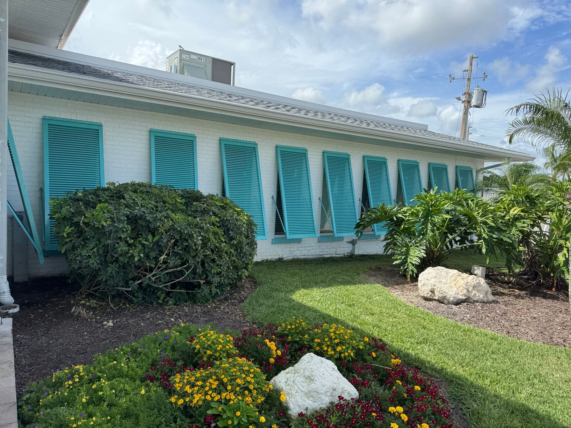 White building with turquoise shutters; colorful flower bed in front.